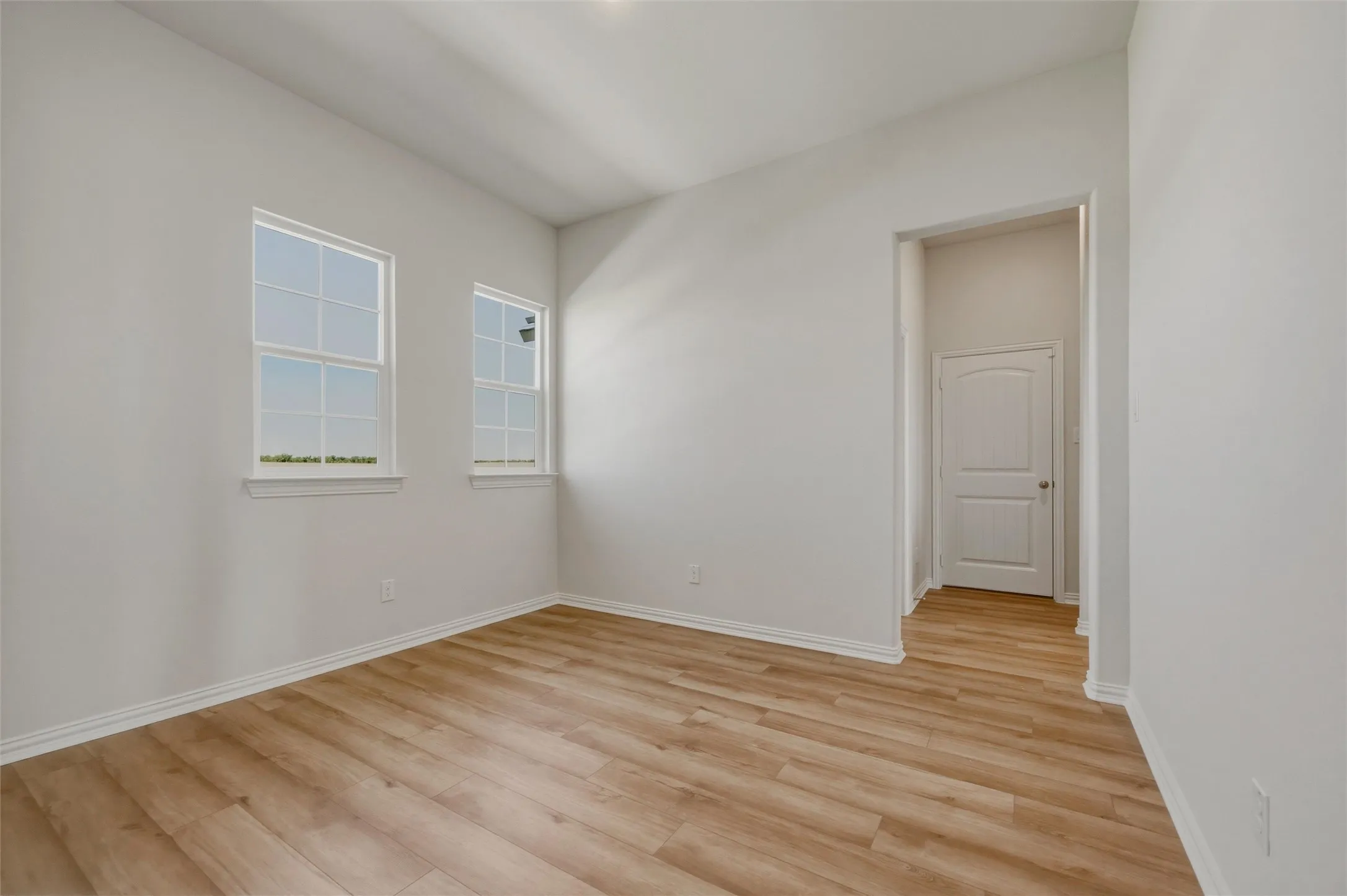 Bright, light-filled bedroom featuring gleaming wood-finish flooring, multiple windows with natural light exposure, and a clean white interior with smooth drywall finishes