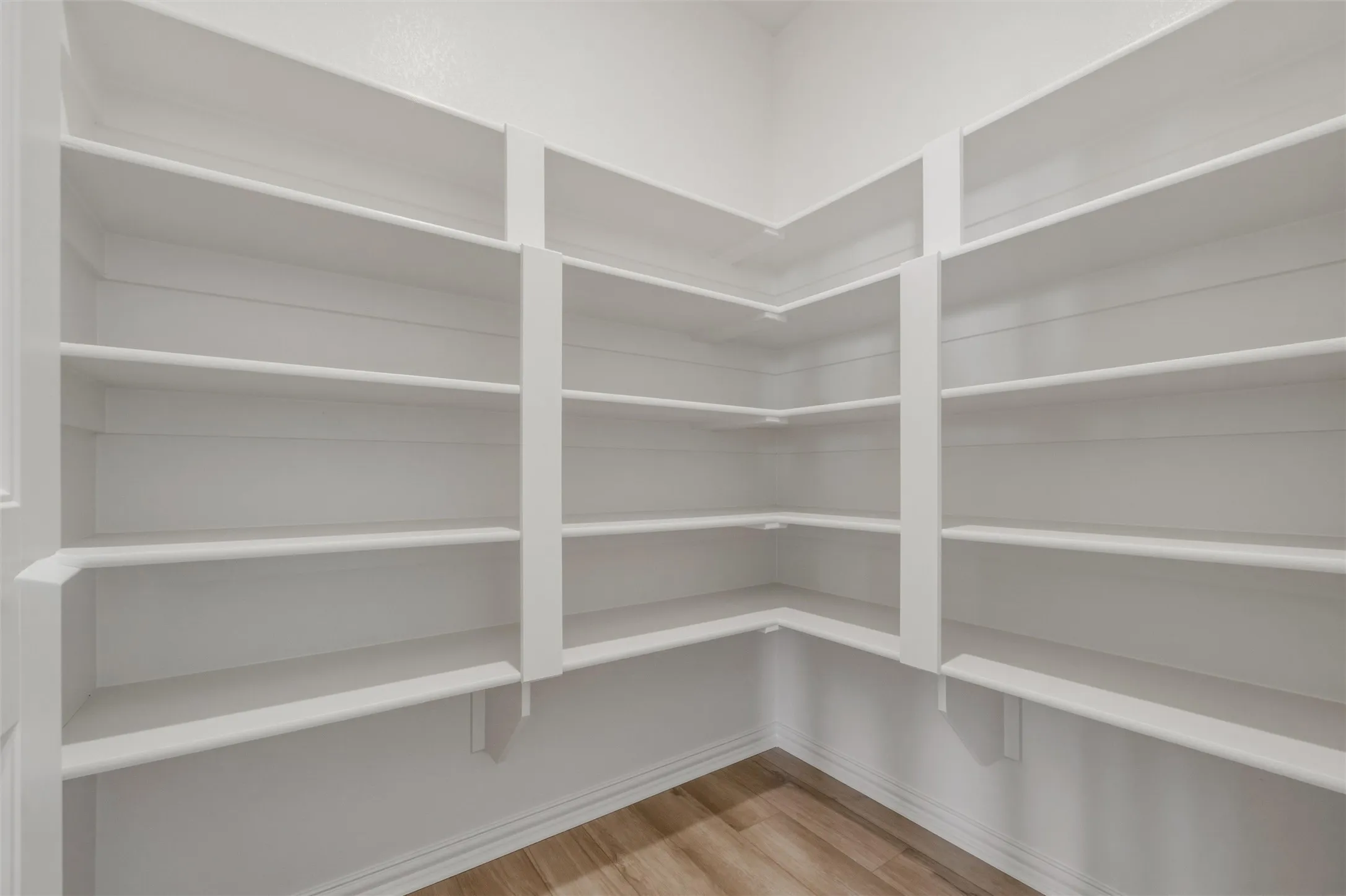 Corner shelving system featuring multiple white shelves and wood-finish flooring