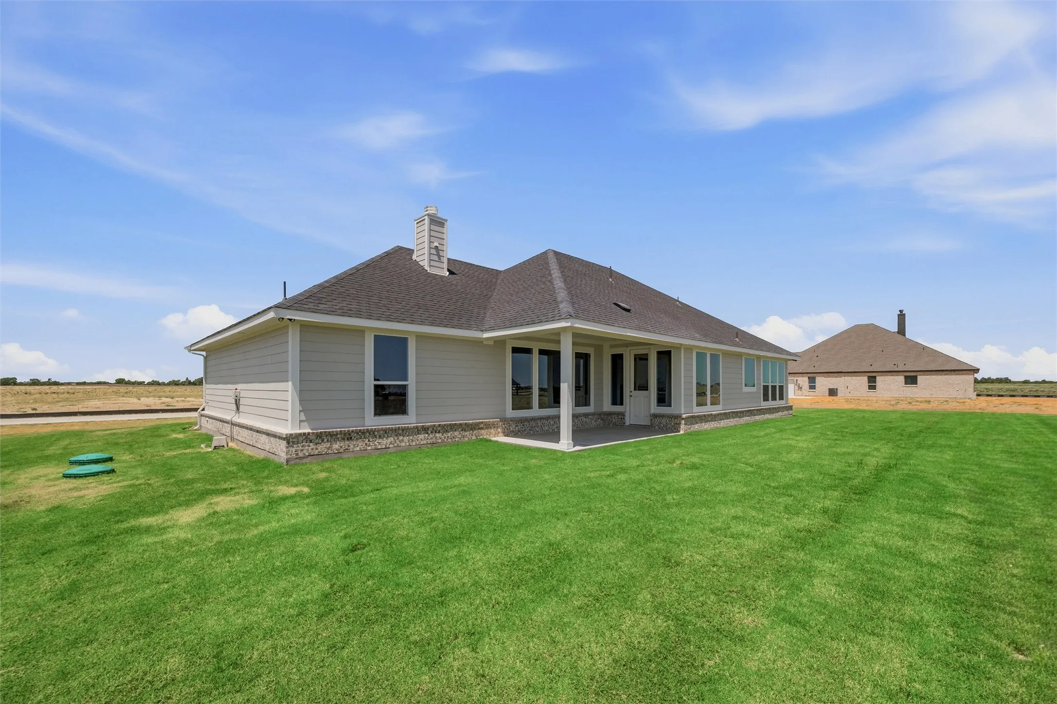 Expansive green lawn with a covered patio, multiple large windows, and a stone accent foundation