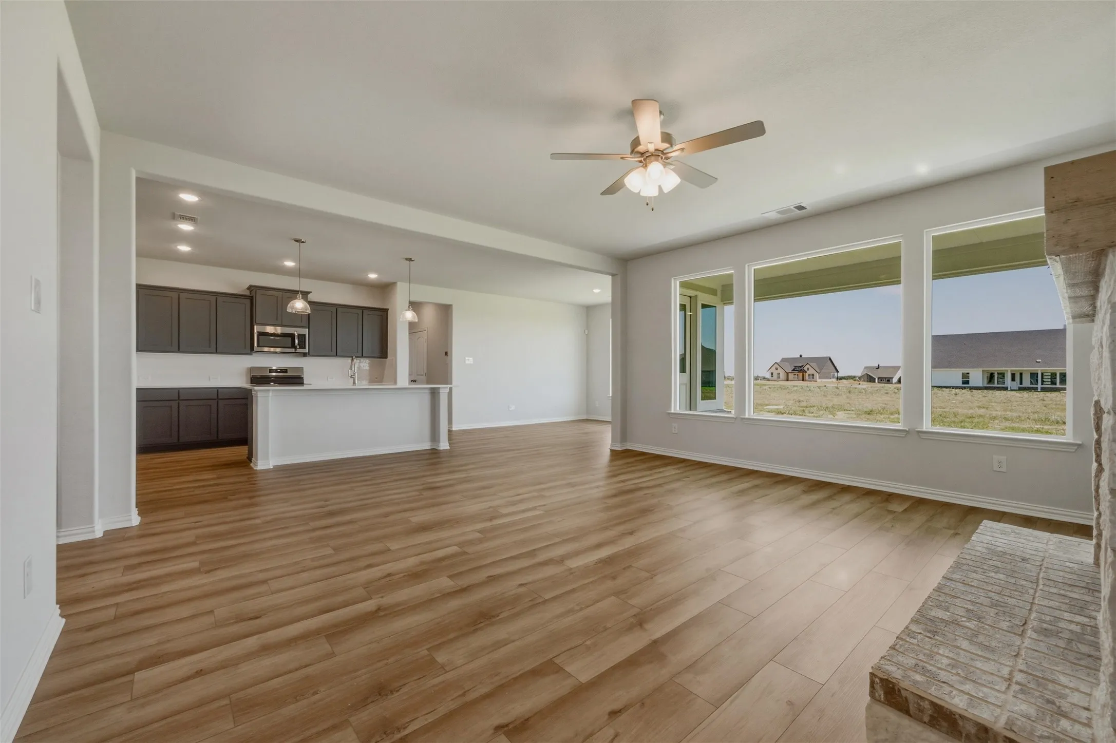 Expansive living area with wood-finish flooring, a stone-clad fireplace, and a ceiling fan