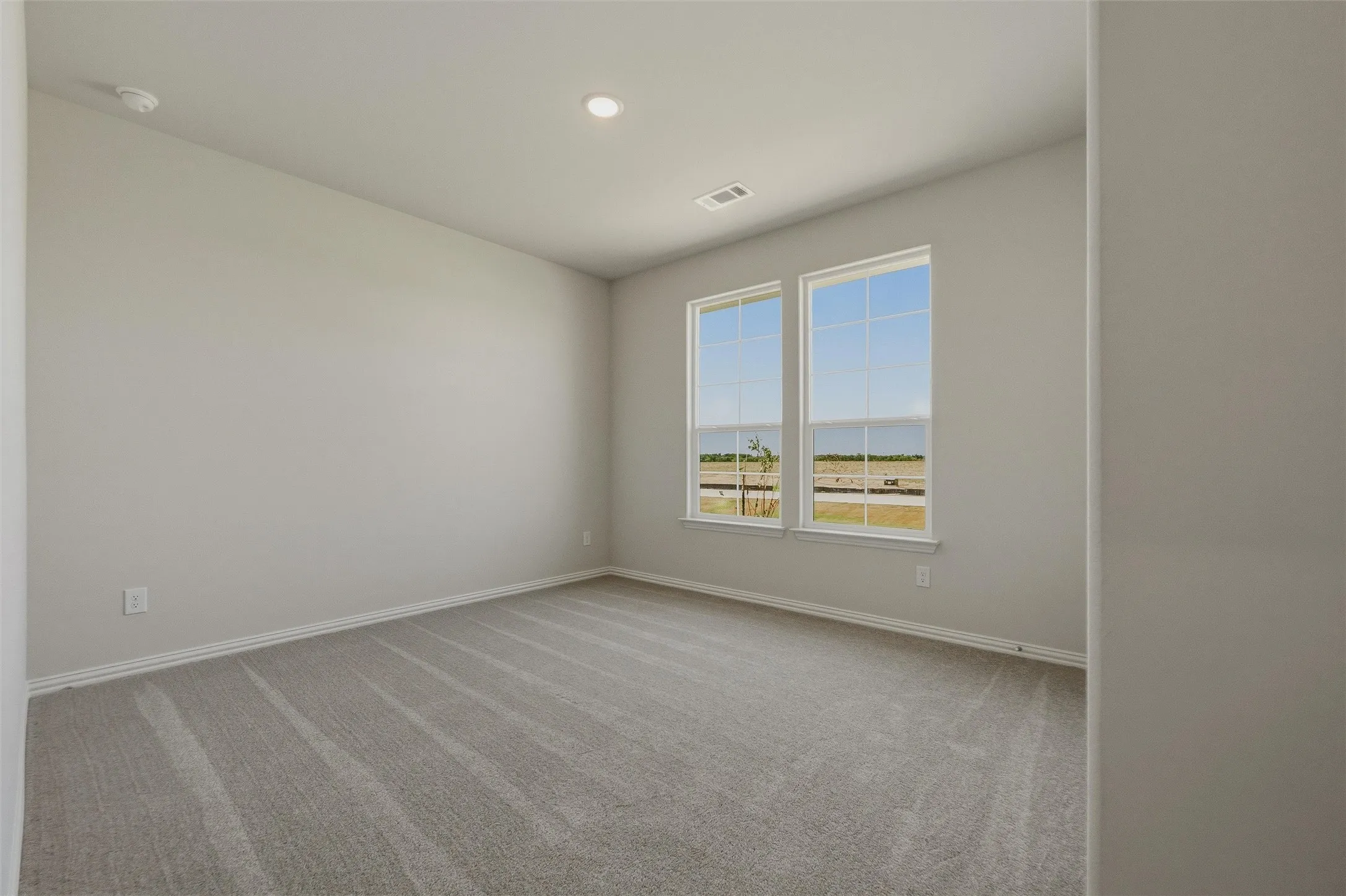 Spacious room featuring neutral paint, gray carpeting, dual windows, and recessed lighting