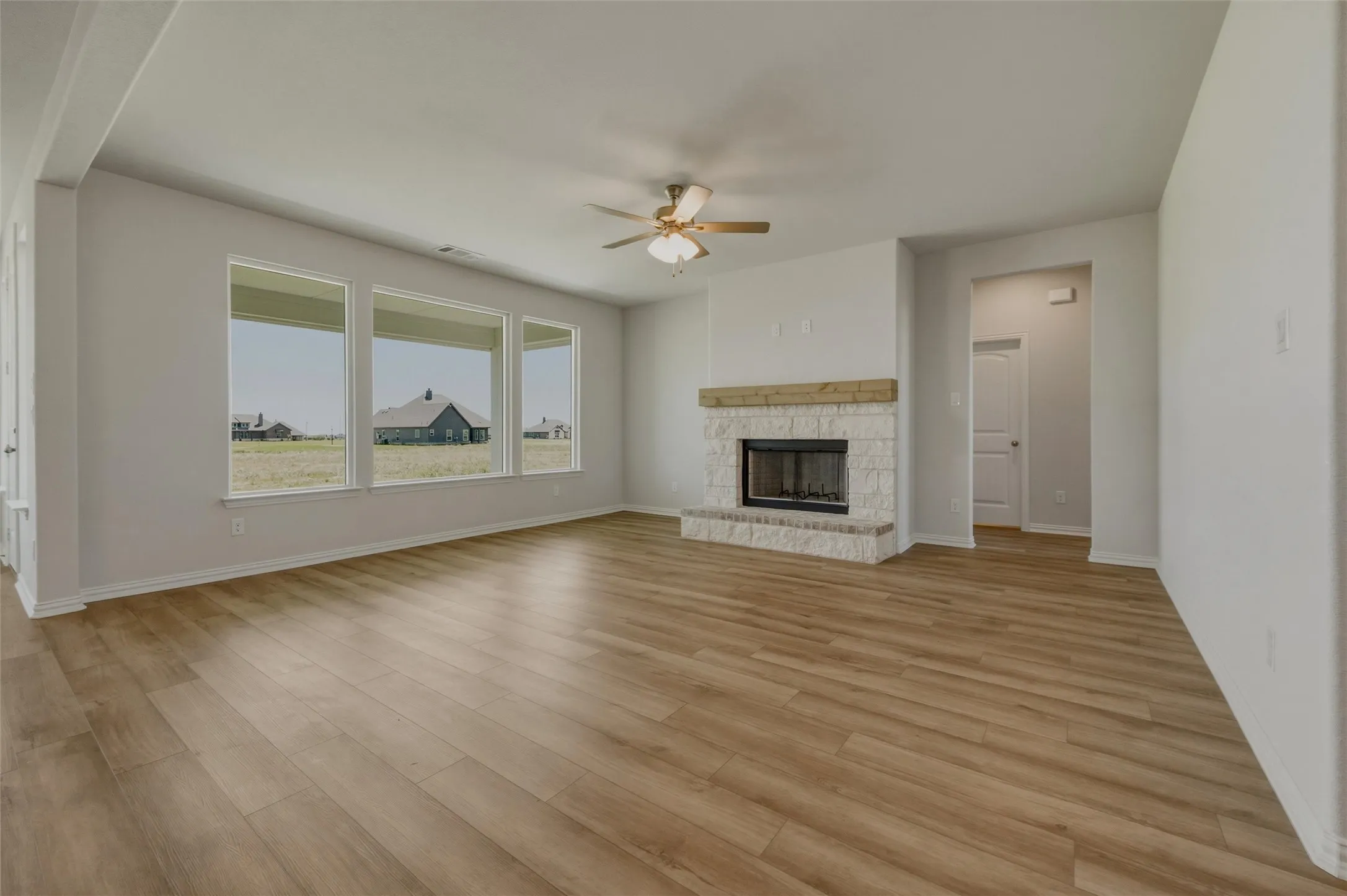 Spacious room featuring wood-finish flooring, a stone-clad fireplace with a wood mantle, and a ceiling fan