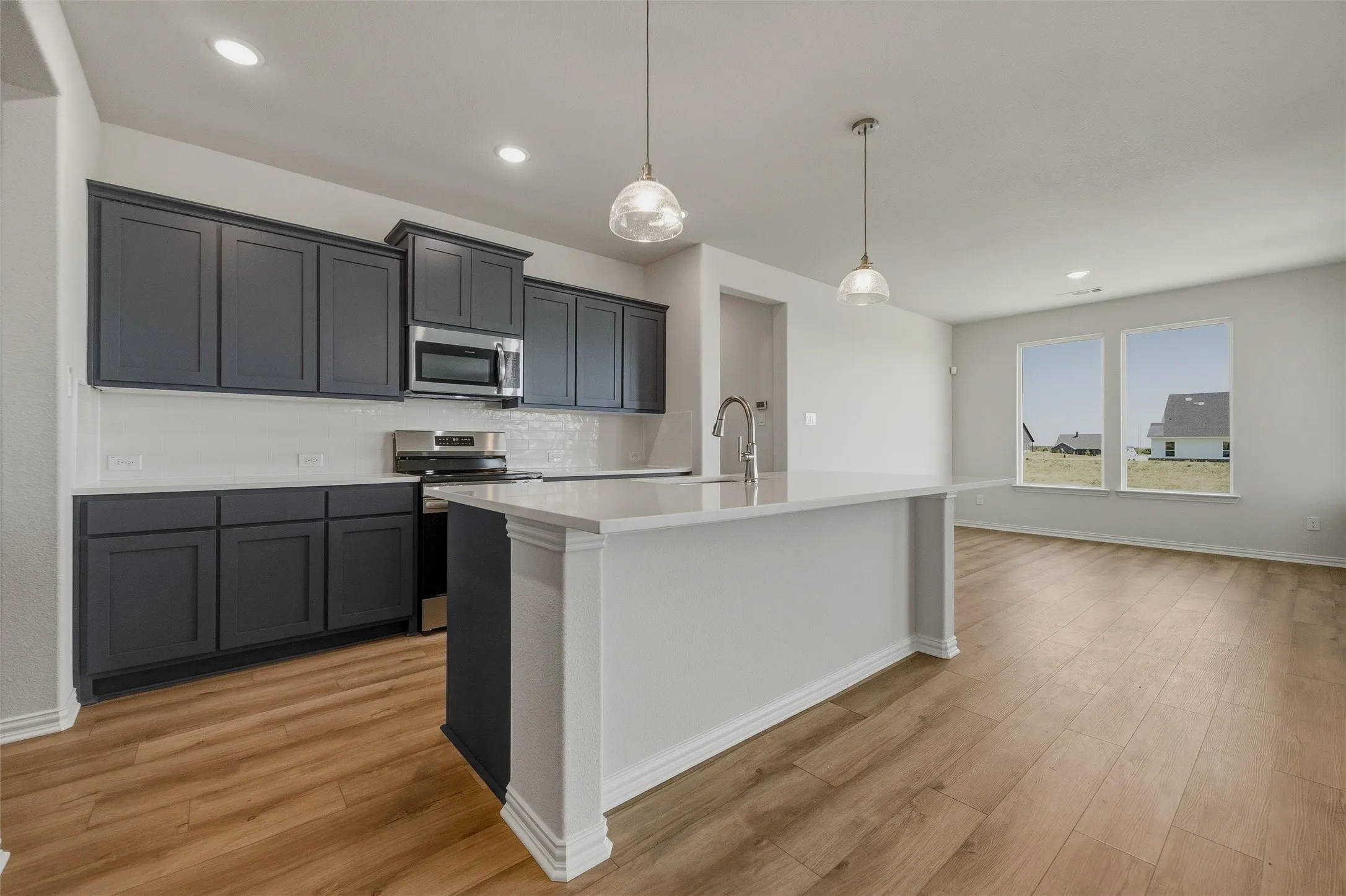 Kitchen featuring dark cabinetry, stainless steel appliances, a white tile backsplash, and a central island with a sink and pendant lighting