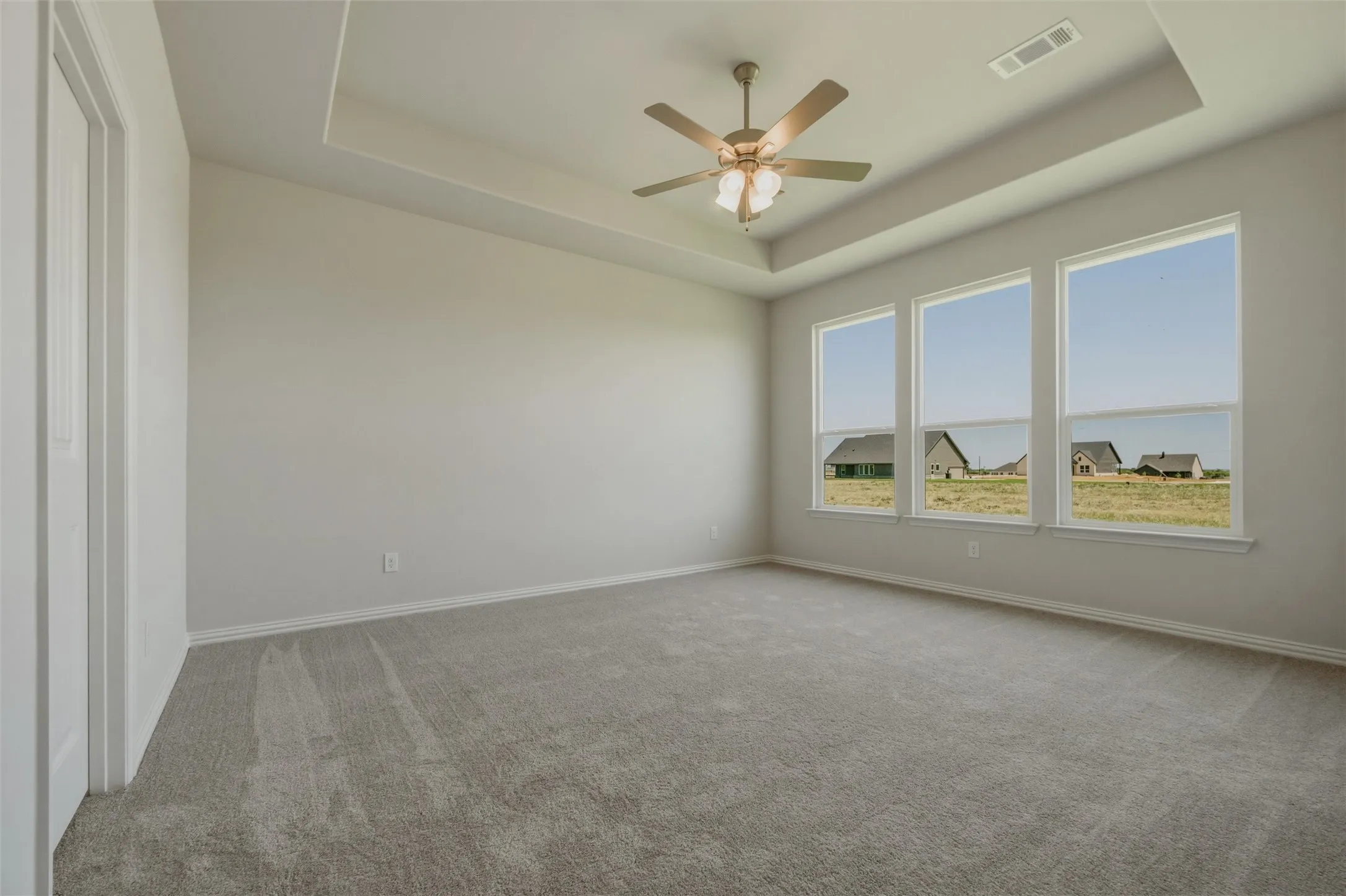 Expansive room featuring a tray ceiling, ceiling fan with light fixture, three large windows, and carpet flooring