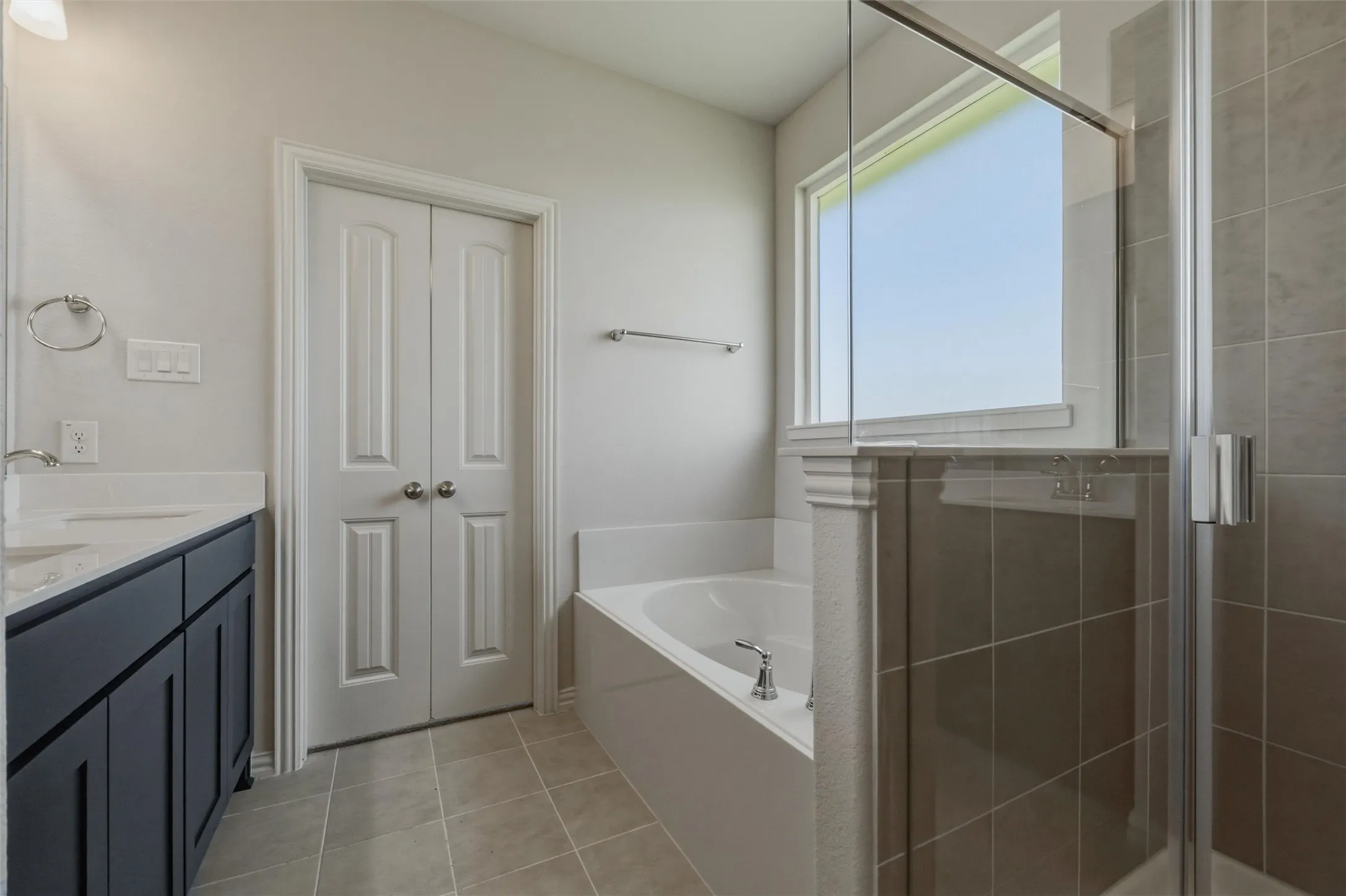 Bathroom featuring a soaking tub, glass-enclosed shower, dual-basin vanity with a light-colored countertop, and a window providing natural light
