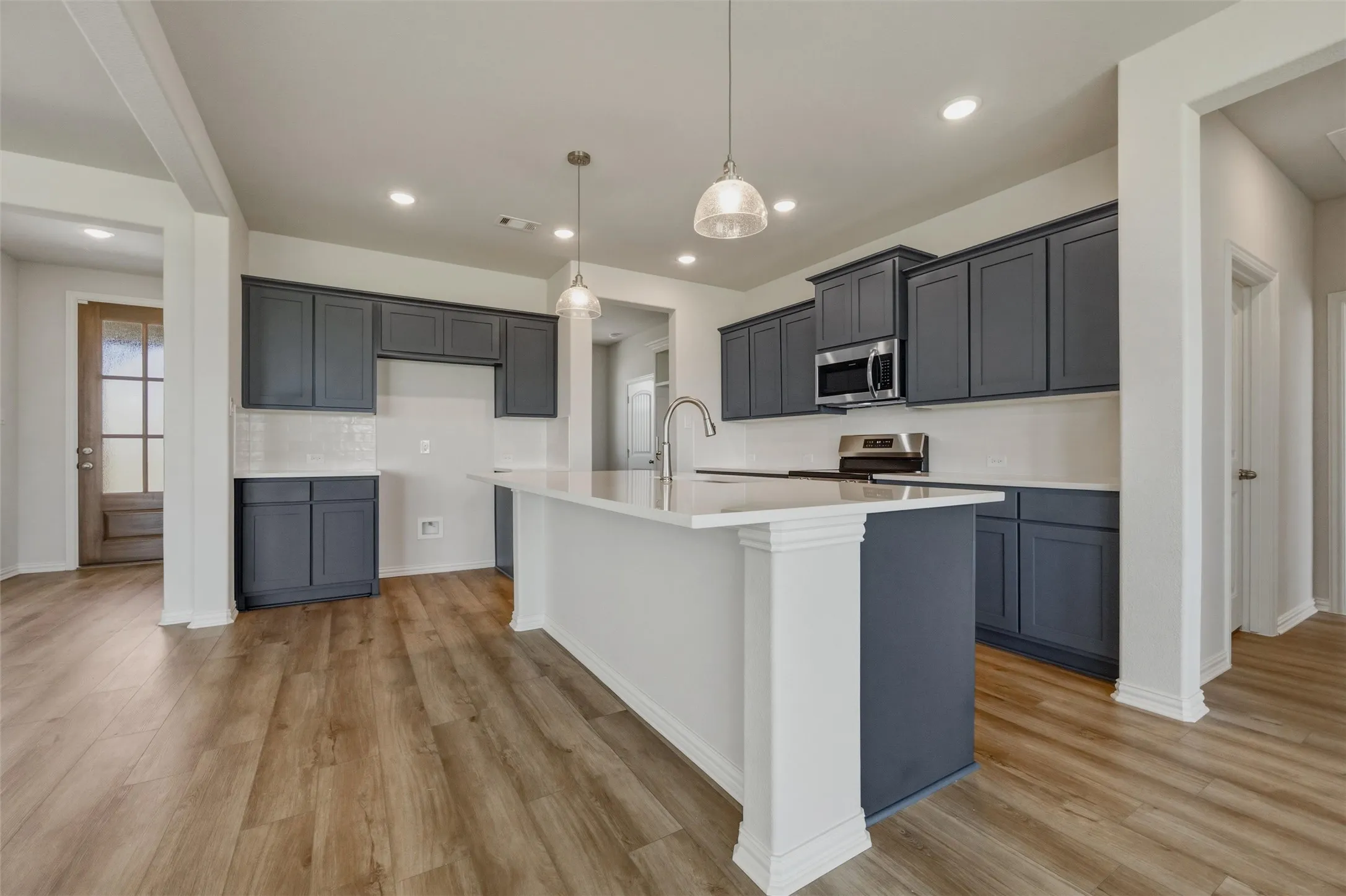 Kitchen featuring a central island with countertop, pendant lighting, wood-finish flooring, and dark cabinetry