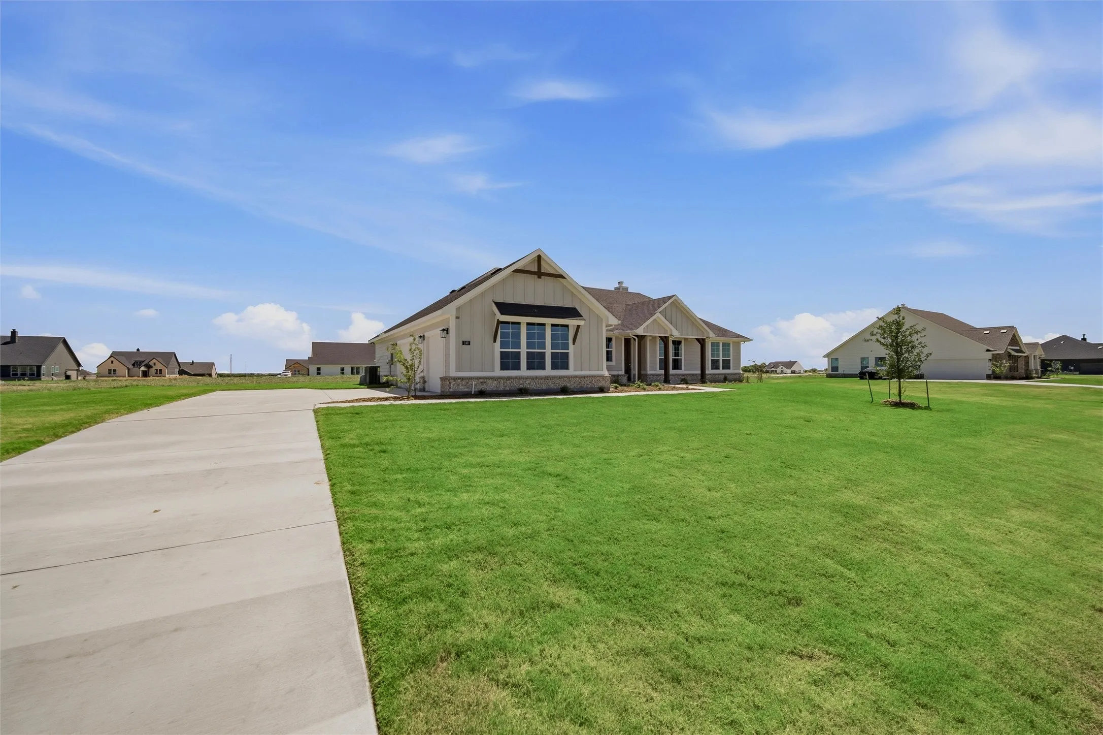 Expansive green lawn with a concrete driveway, board and batten siding, stone facade accents, and a covered front porch