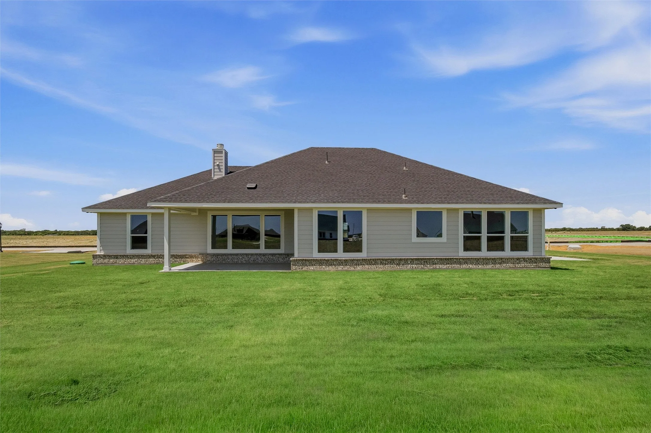 Expansive green lawn surrounds the residence, featuring a covered patio and multiple large windows