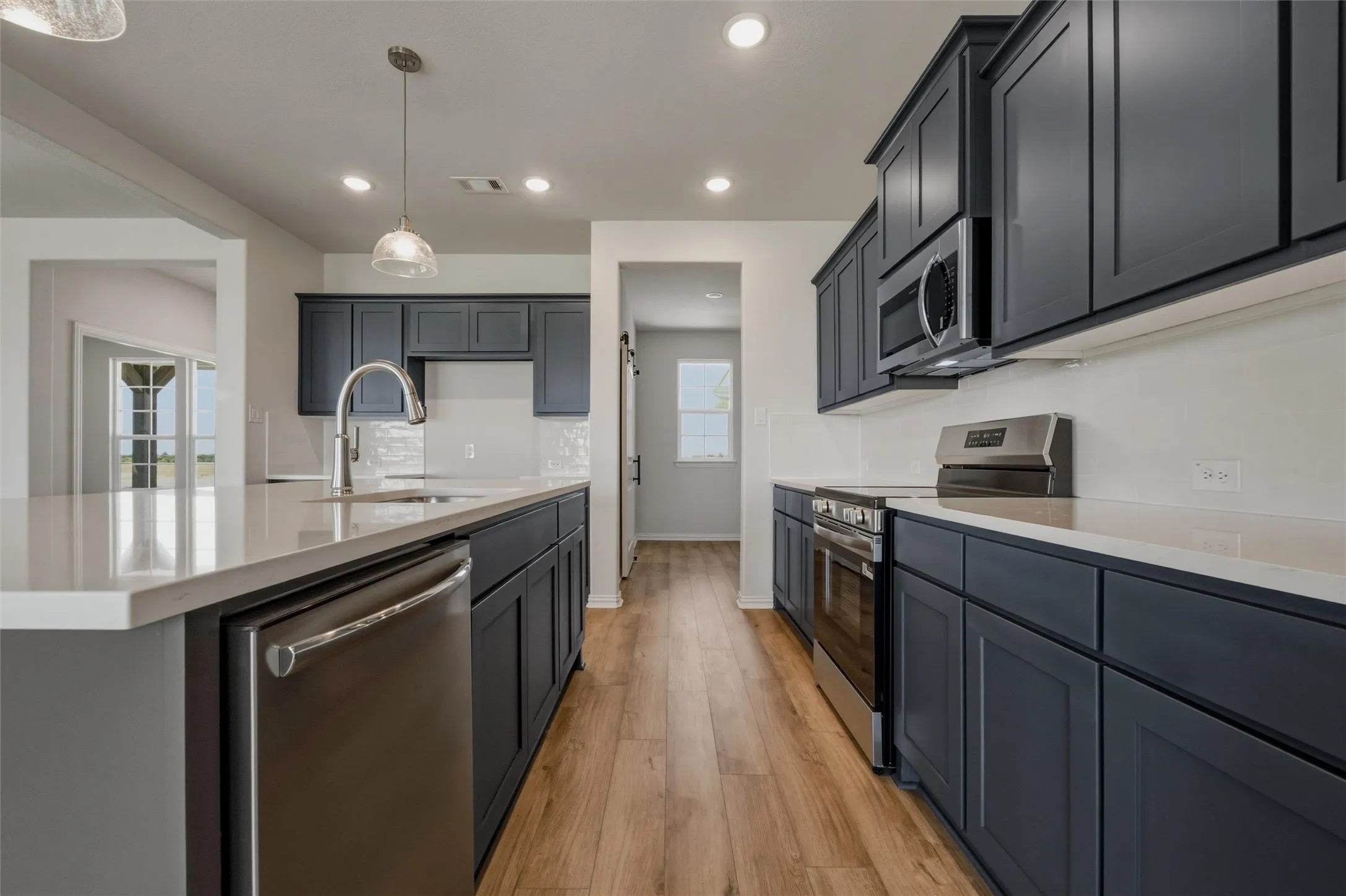 Kitchen featuring dark wood cabinetry, light-toned countertops, stainless steel appliances, a tile backsplash, and wood-finish flooring