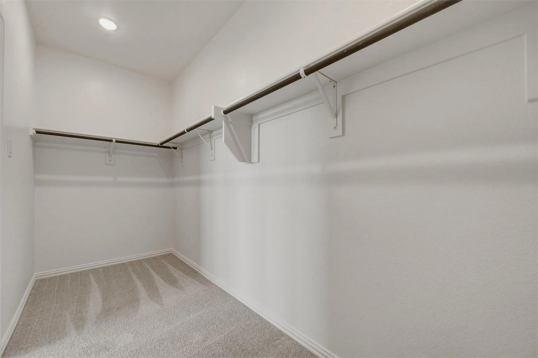 Recessed ceiling lighting, gray carpet flooring, white painted walls, and built-in closet shelving with hanging rods