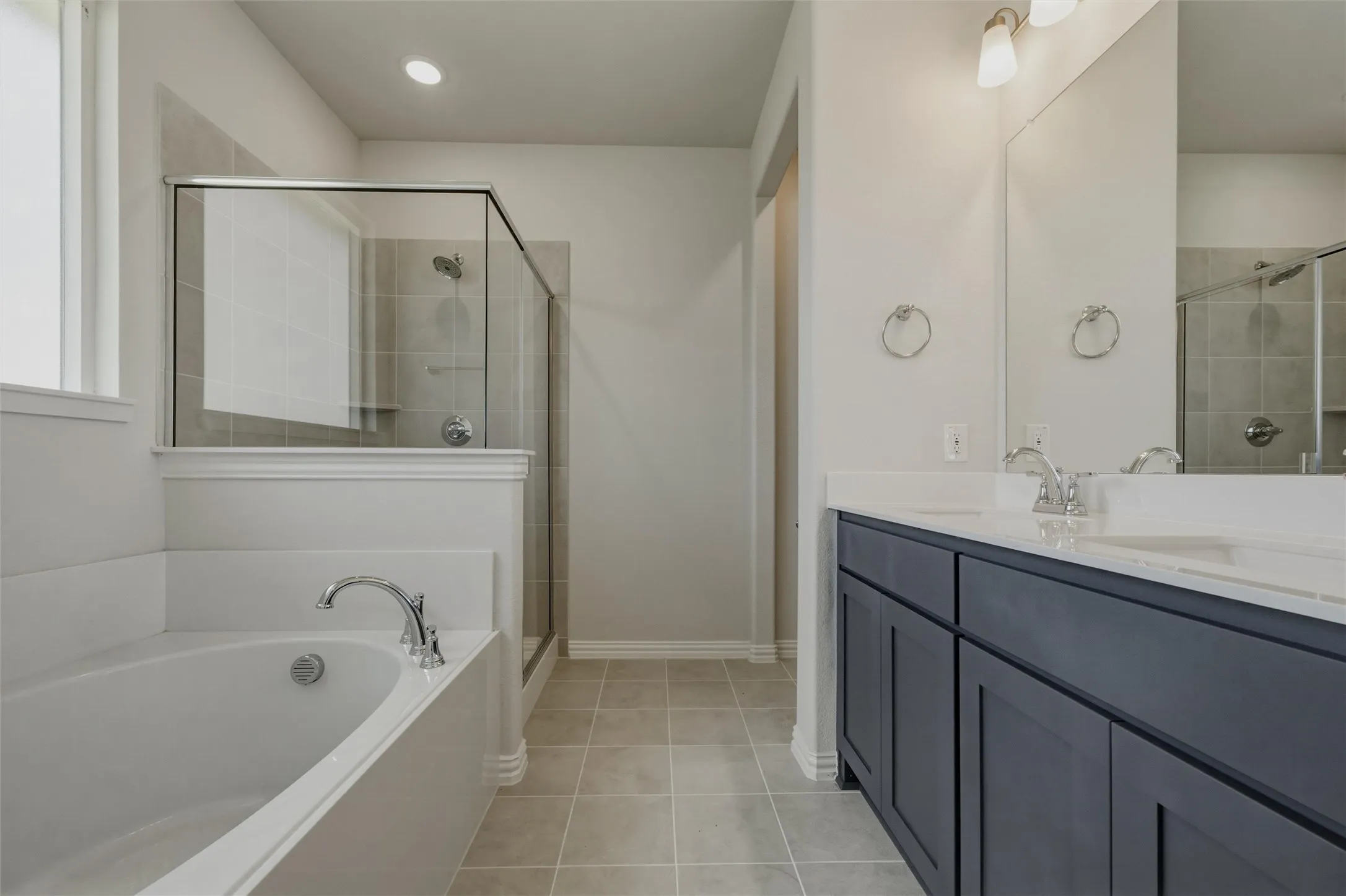 Dual vanity with white countertops, deep soaking tub, glass-enclosed shower, and tiled flooring