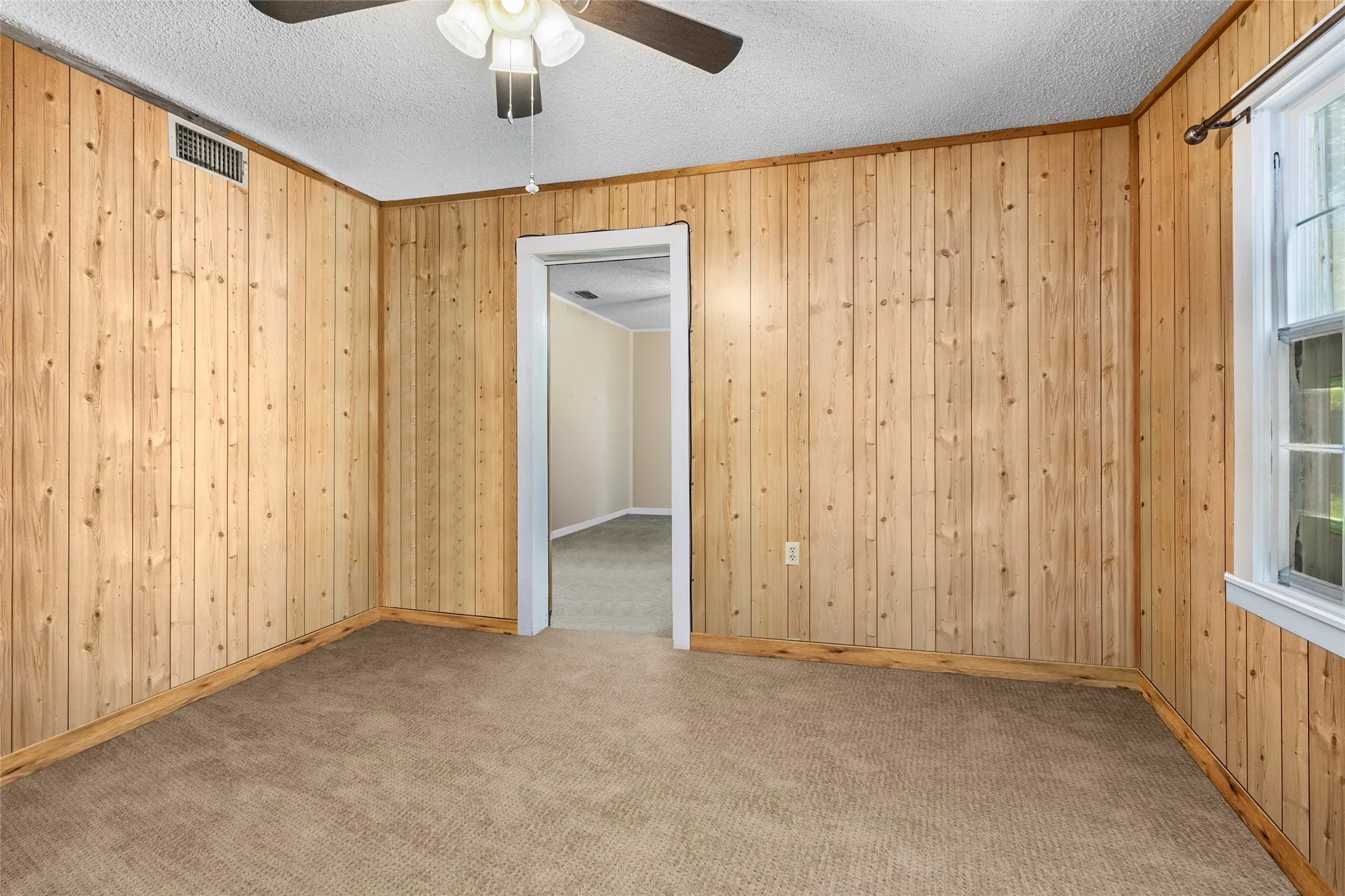 Carpeted spare room with wooden walls, ceiling fan, and a textured ceiling
