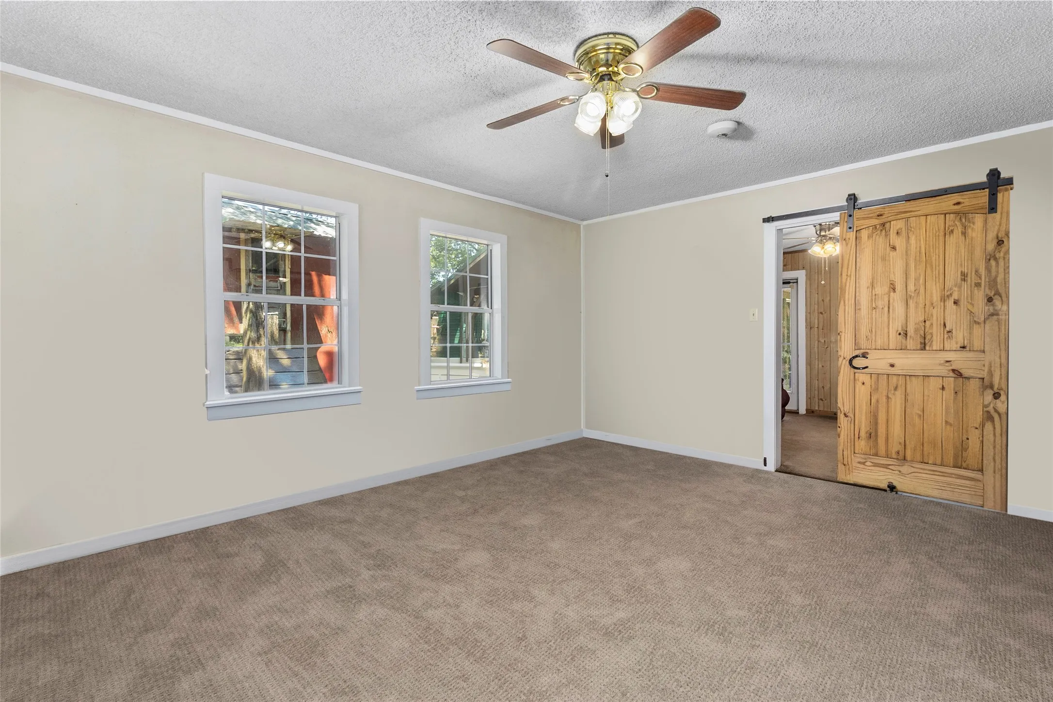 Spare room featuring ceiling fan, a barn door, a textured ceiling, carpet, and ornamental molding