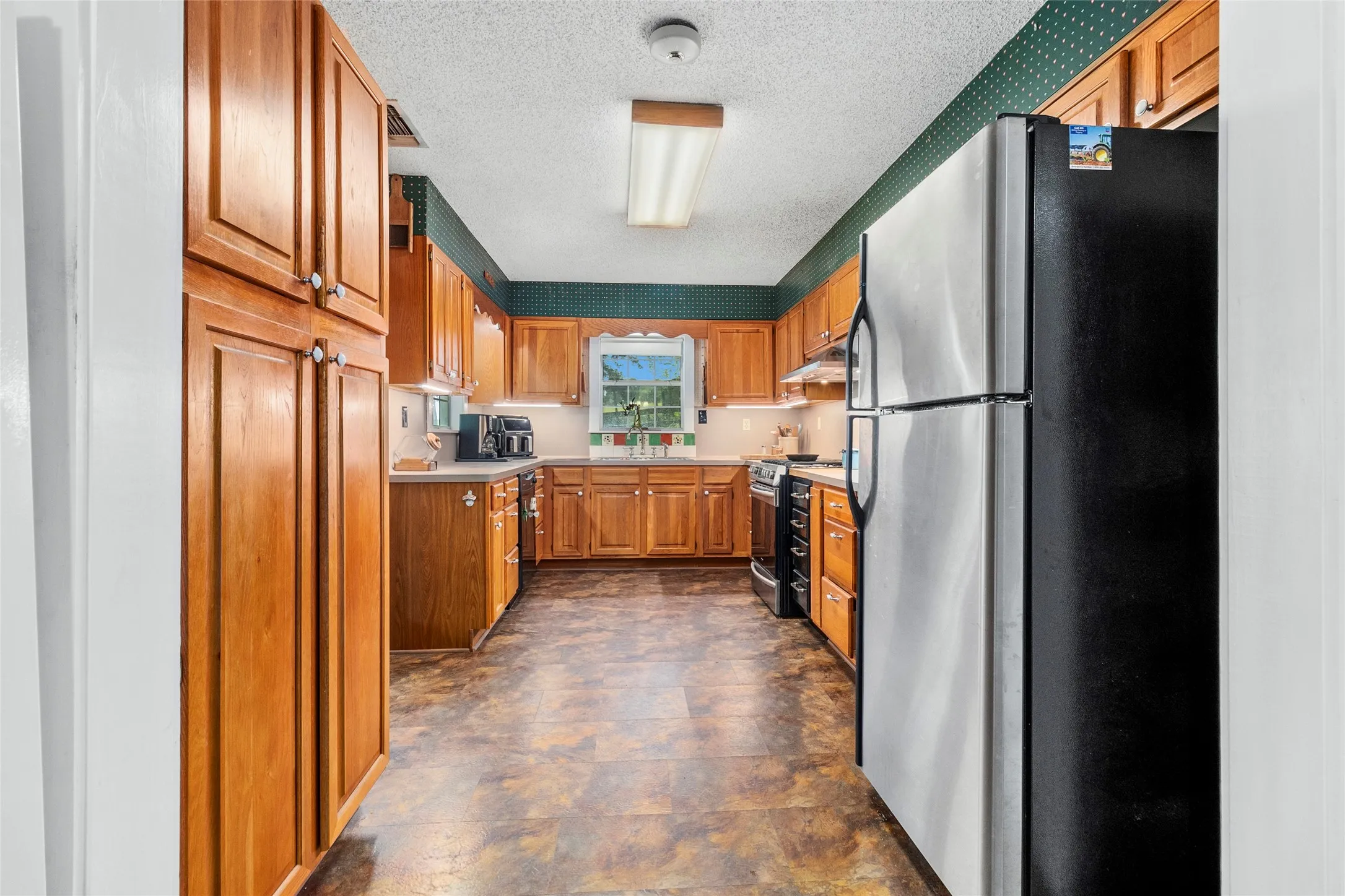 Kitchen featuring sink, a textured ceiling, dark tile floors, and appliances with stainless steel finishes