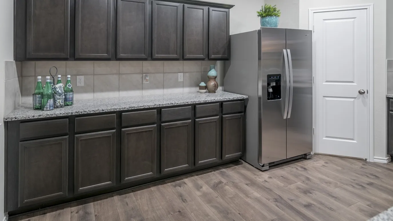 Kitchen area featuring dark wood cabinetry, light-colored countertops, a neutral-toned tiled backsplash, and stainless steel refrigerator