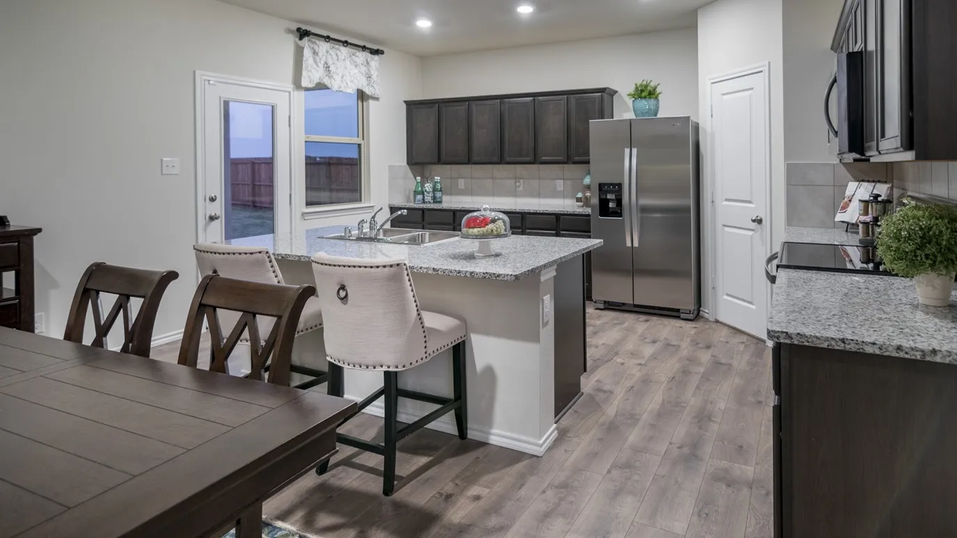 The kitchen features a central island with a granite countertop, dark wood cabinetry, a stainless steel refrigerator, and wood-look flooring