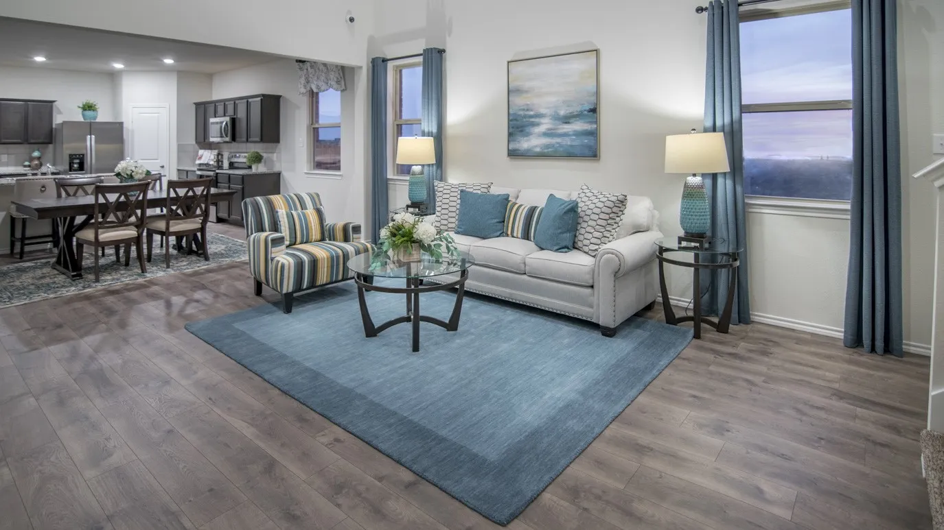 The open concept living area features wood-look flooring and a bright window with blue curtains