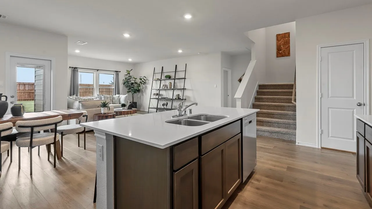 Open-concept living area featuring light wood-style flooring, an island with a sink and white countertop, and a view of the backyard through a glass-paneled door
