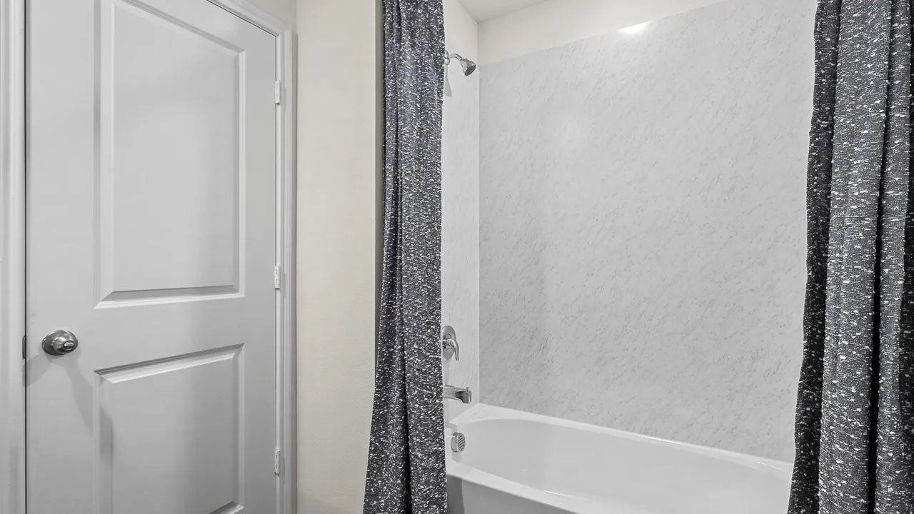 Bathroom featuring a white tub, shower with light-colored wall surround, and a white paneled door