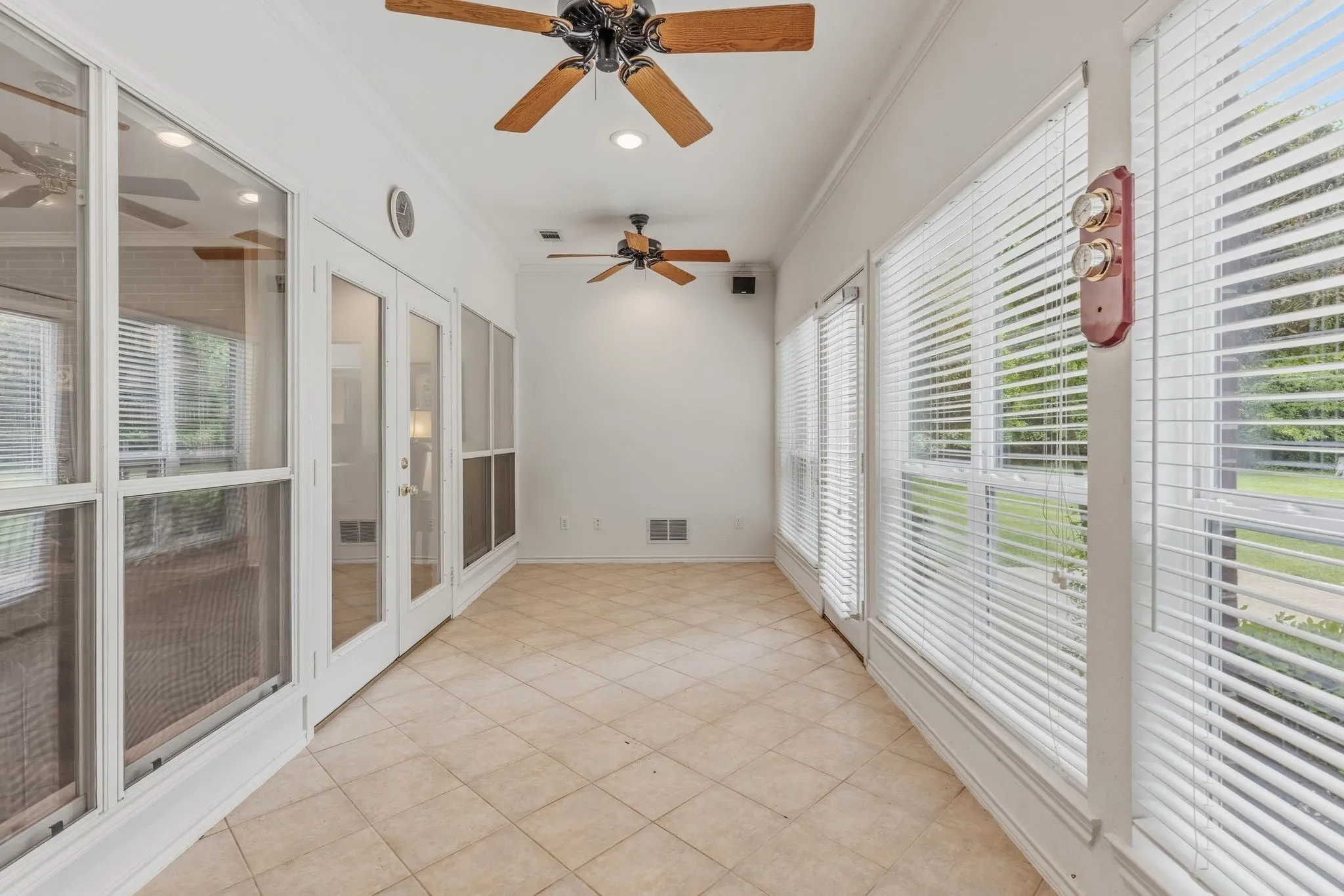 Light-filled sunroom featuring tiled flooring, extensive windows with blinds, and two ceiling fans