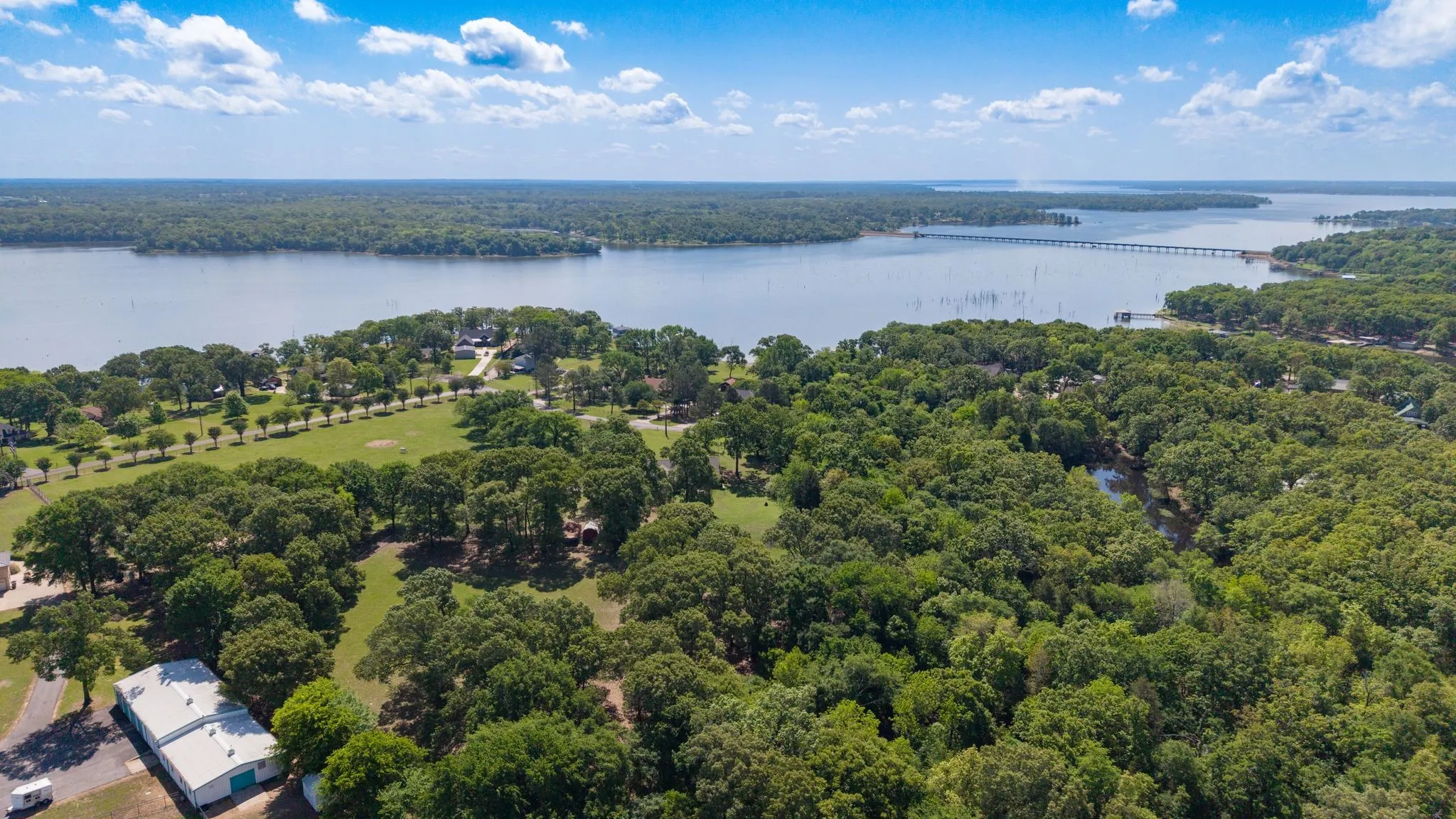 Expansive aerial view of the property's lush, green surroundings, featuring extensive tree coverage and proximity to a large body of water