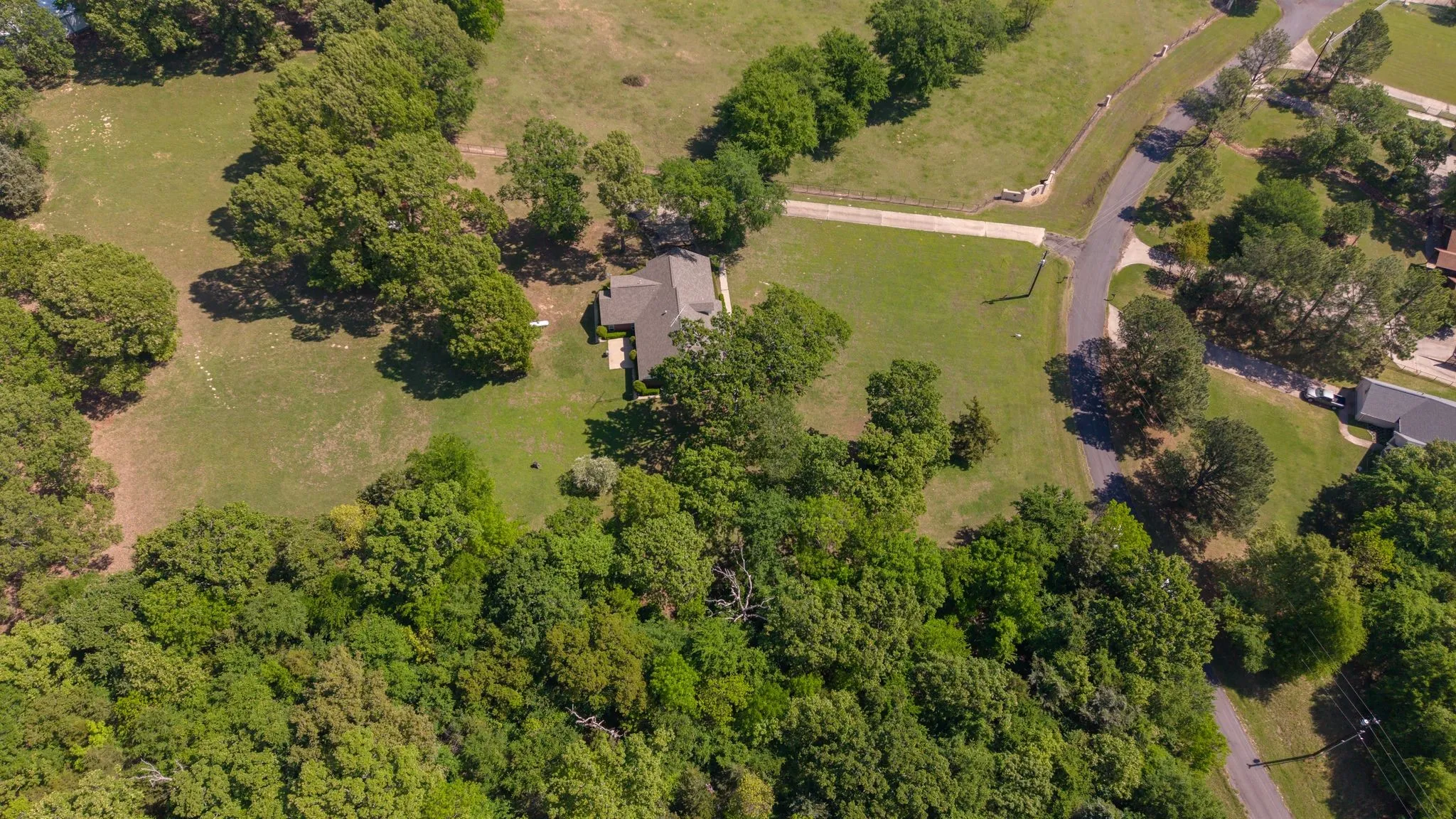 An aerial view showcases the property with a brown roof, surrounded by expansive green lawns and mature trees