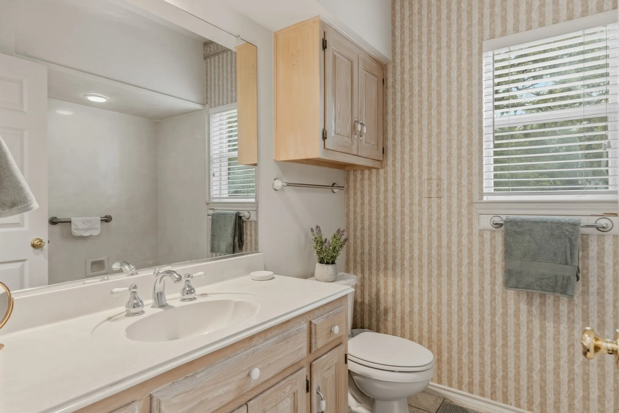 Bathroom featuring a vanity with a white countertop and a built-in sink, a wall-mounted mirror, and a window with blinds