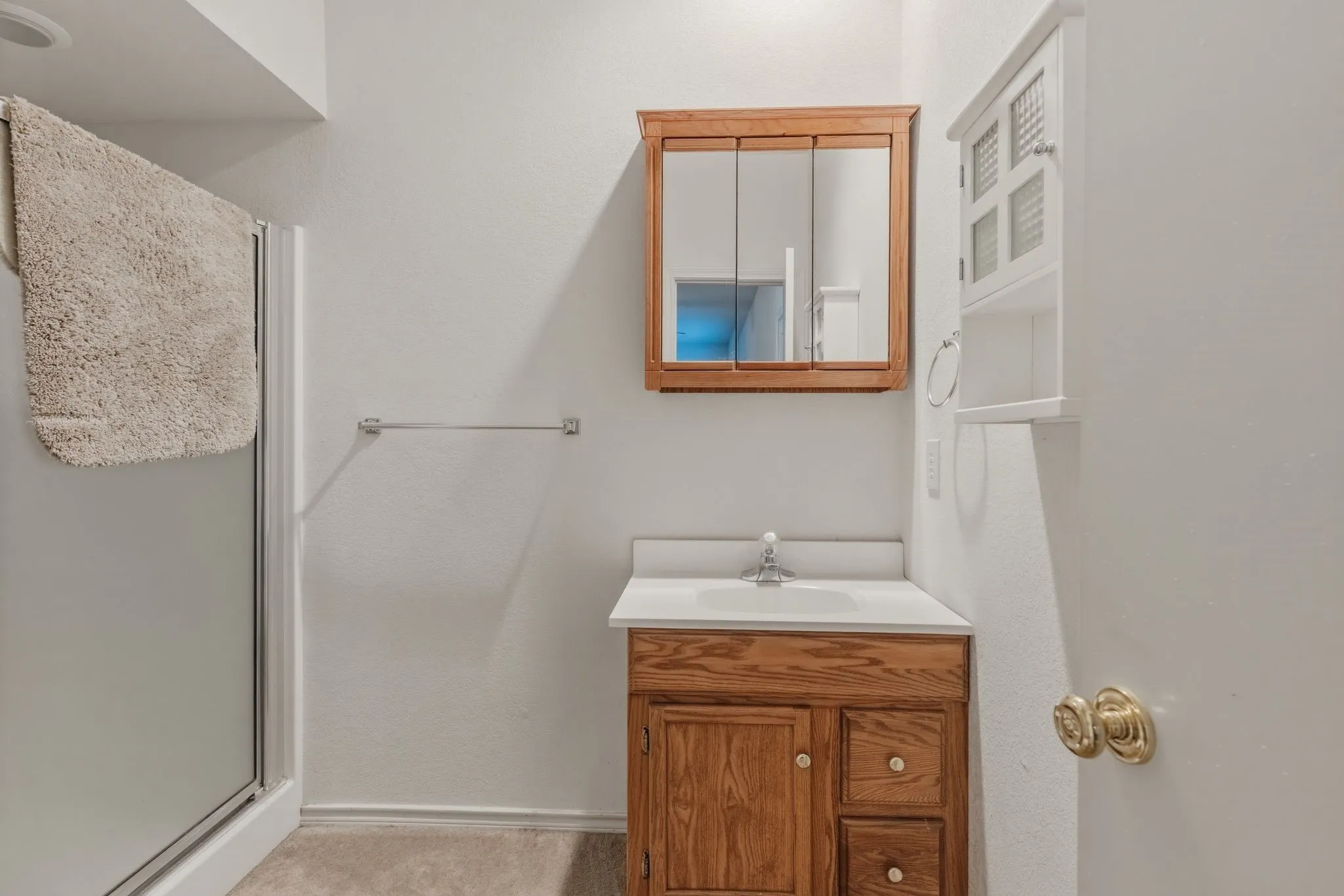 This bathroom features a shower with a clear glass enclosure, a wooden vanity with a white countertop and an integrated sink, and a mirrored medicine cabinet located off of the study