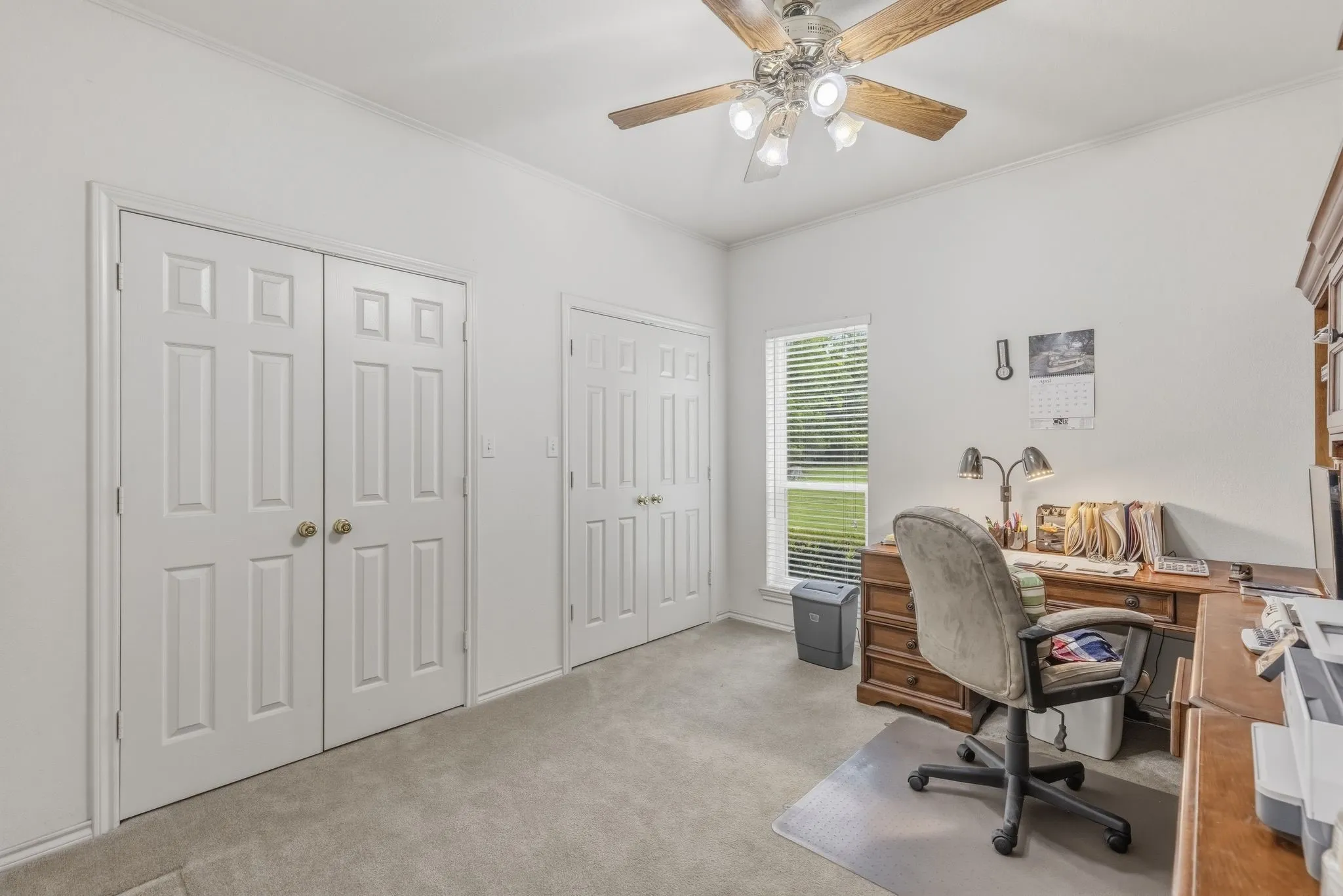 This room features plush carpet flooring, a ceiling fan with light fixture, and white painted walls
