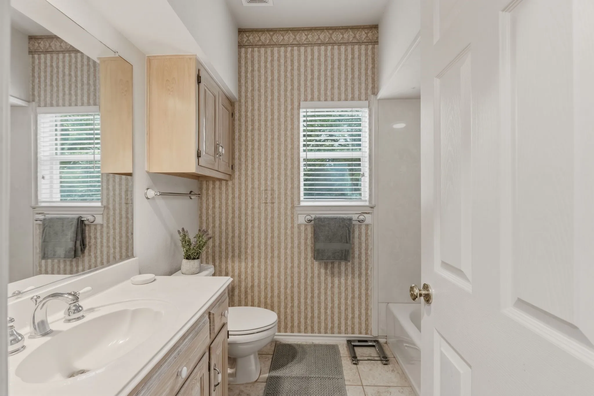 The bathroom features a vanity with a white countertop and an integrated sink, a built-in toilet, a window with blinds, and a bathtub with a shower
