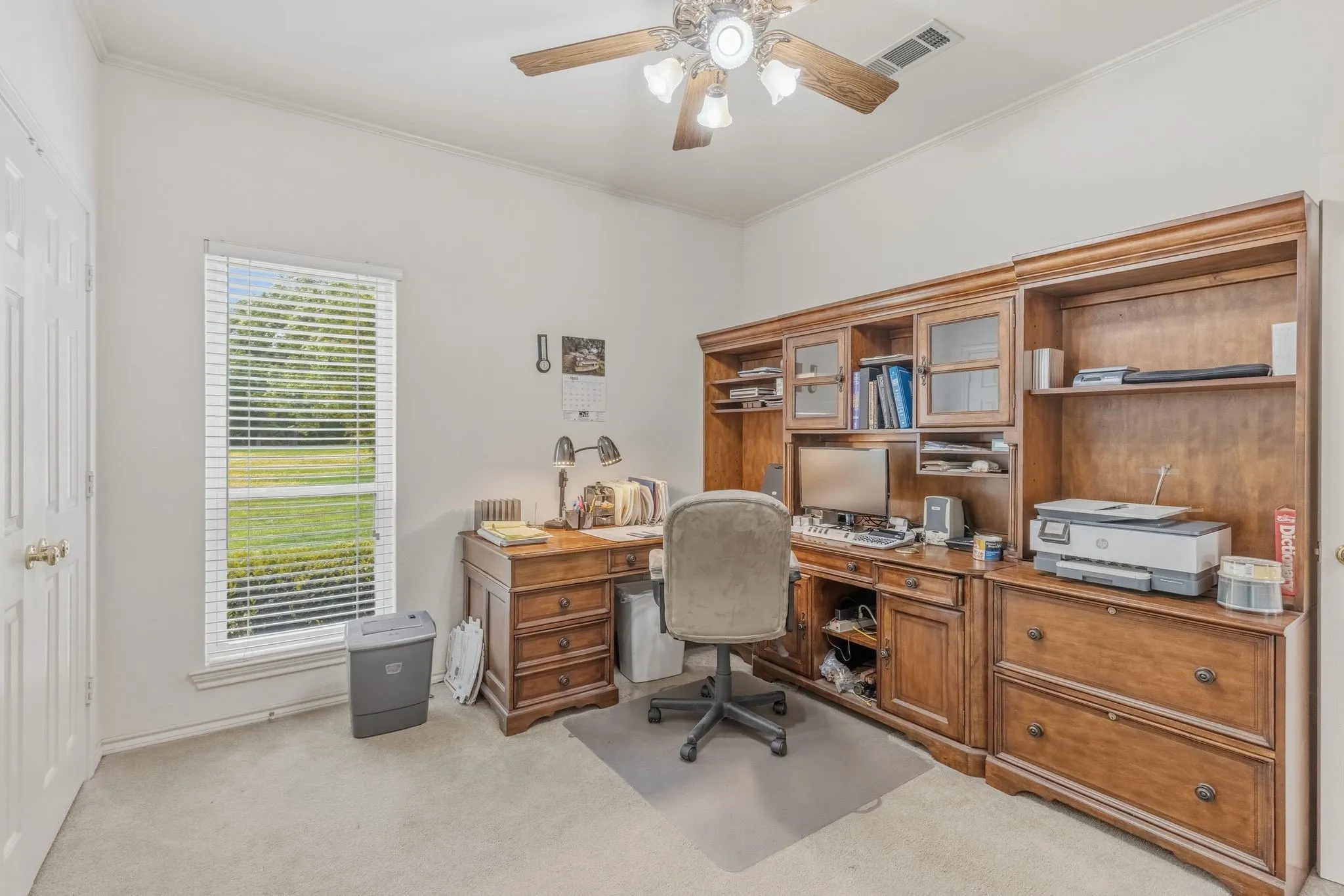 The property features a room with a ceiling fan, a window providing a view of green outdoor space, and light-colored carpeting