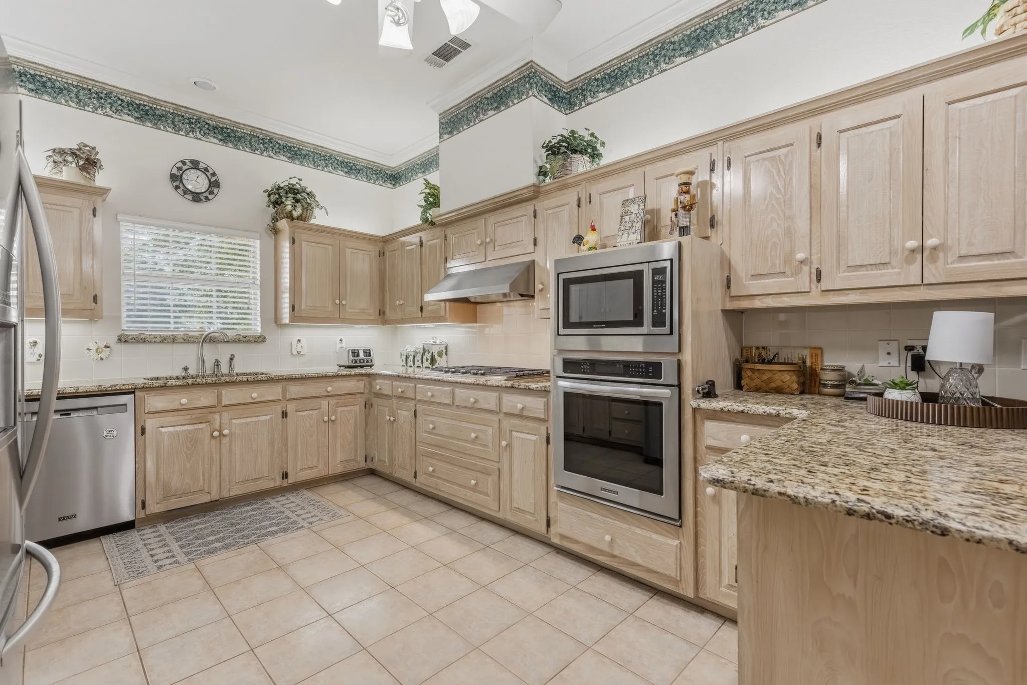 The kitchen features extensive cabinetry, light-colored granite countertops, and stainless steel appliances including a built-in oven and microwave