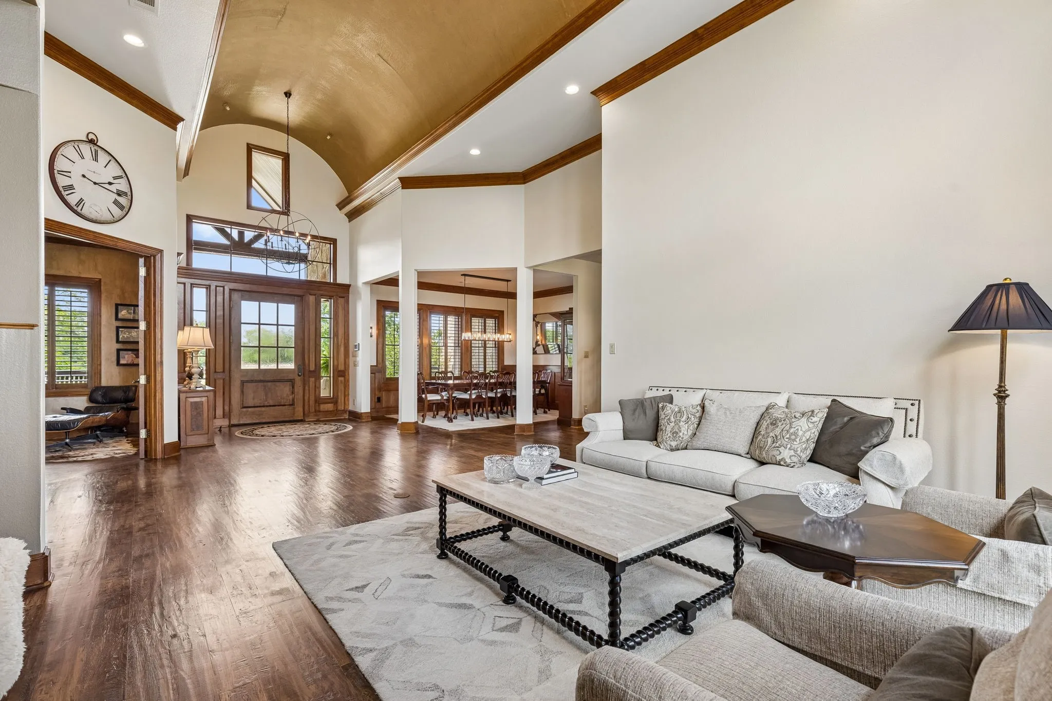 Spacious entryway featuring hardwood floors, a wooden arched door with glass panes, and a vaulted ceiling with wood beams