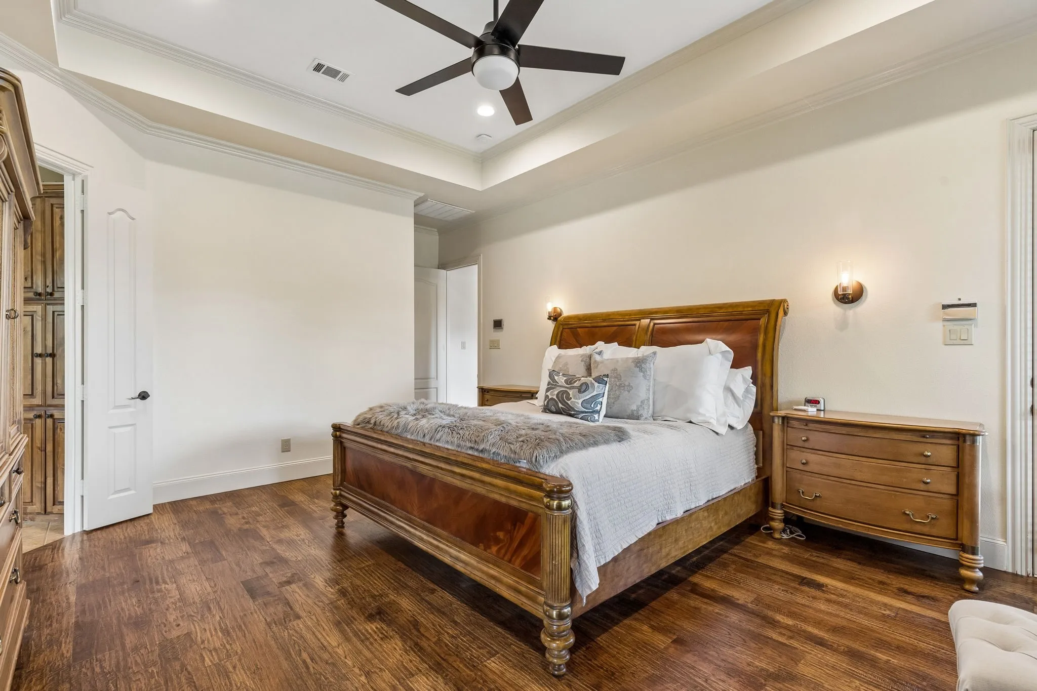 Bedroom featuring hardwood floors, a tray ceiling with recessed lighting and a ceiling fan, and wall sconces