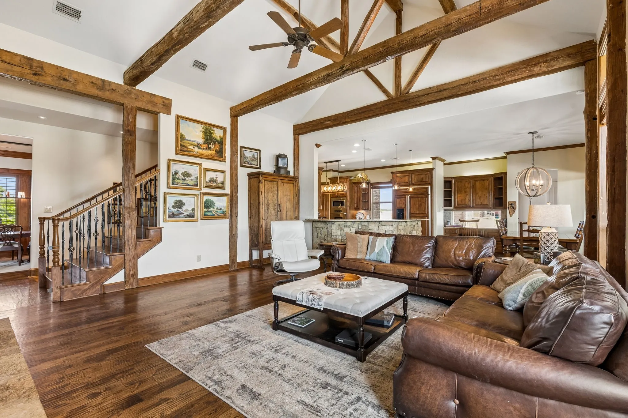 The spacious living area features high ceilings with exposed wooden beams, hardwood flooring, and a staircase with an ornate railing