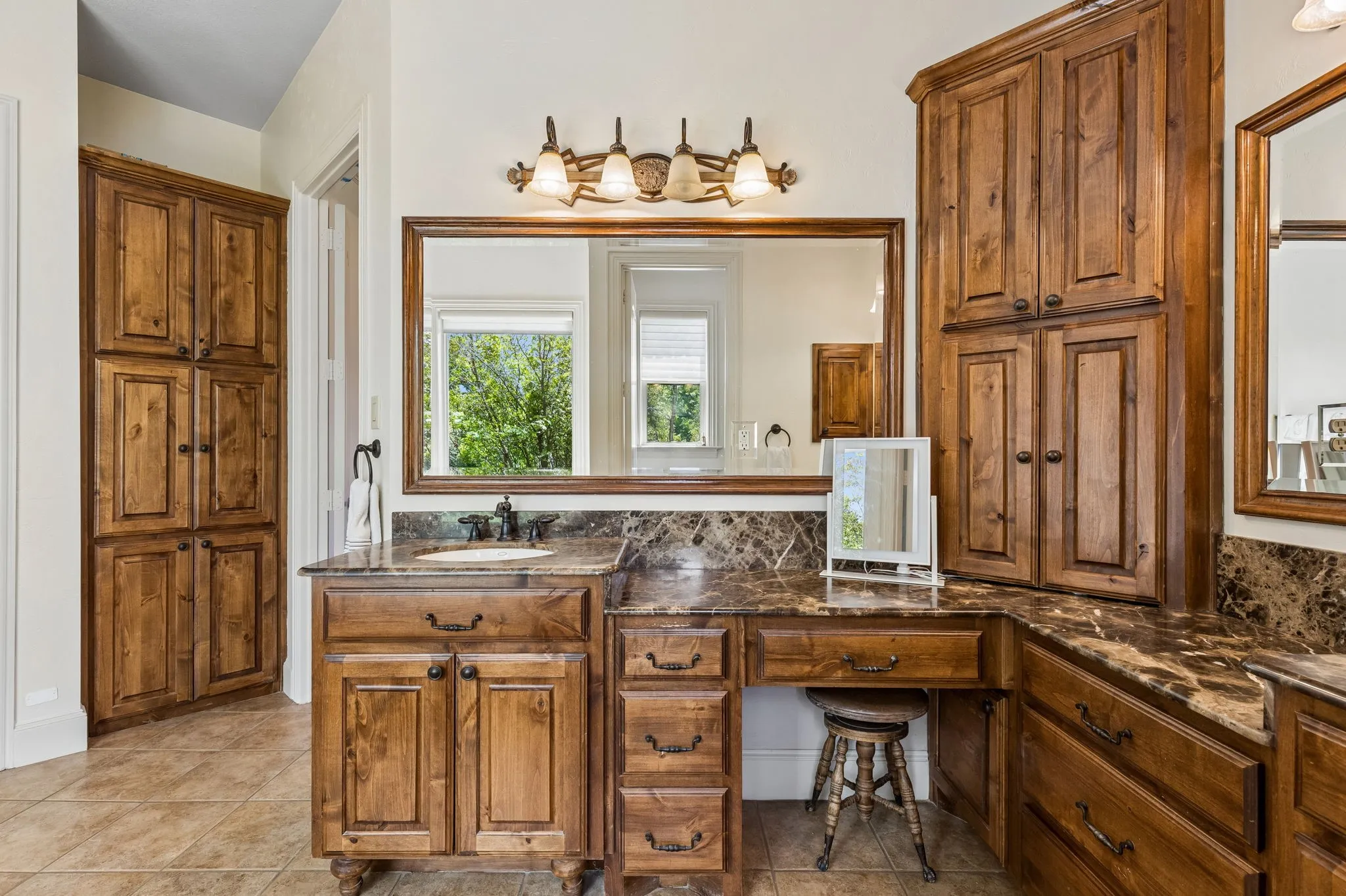 Bathroom featuring extensive wood cabinetry, marble countertops, and a large mirror with integrated lighting