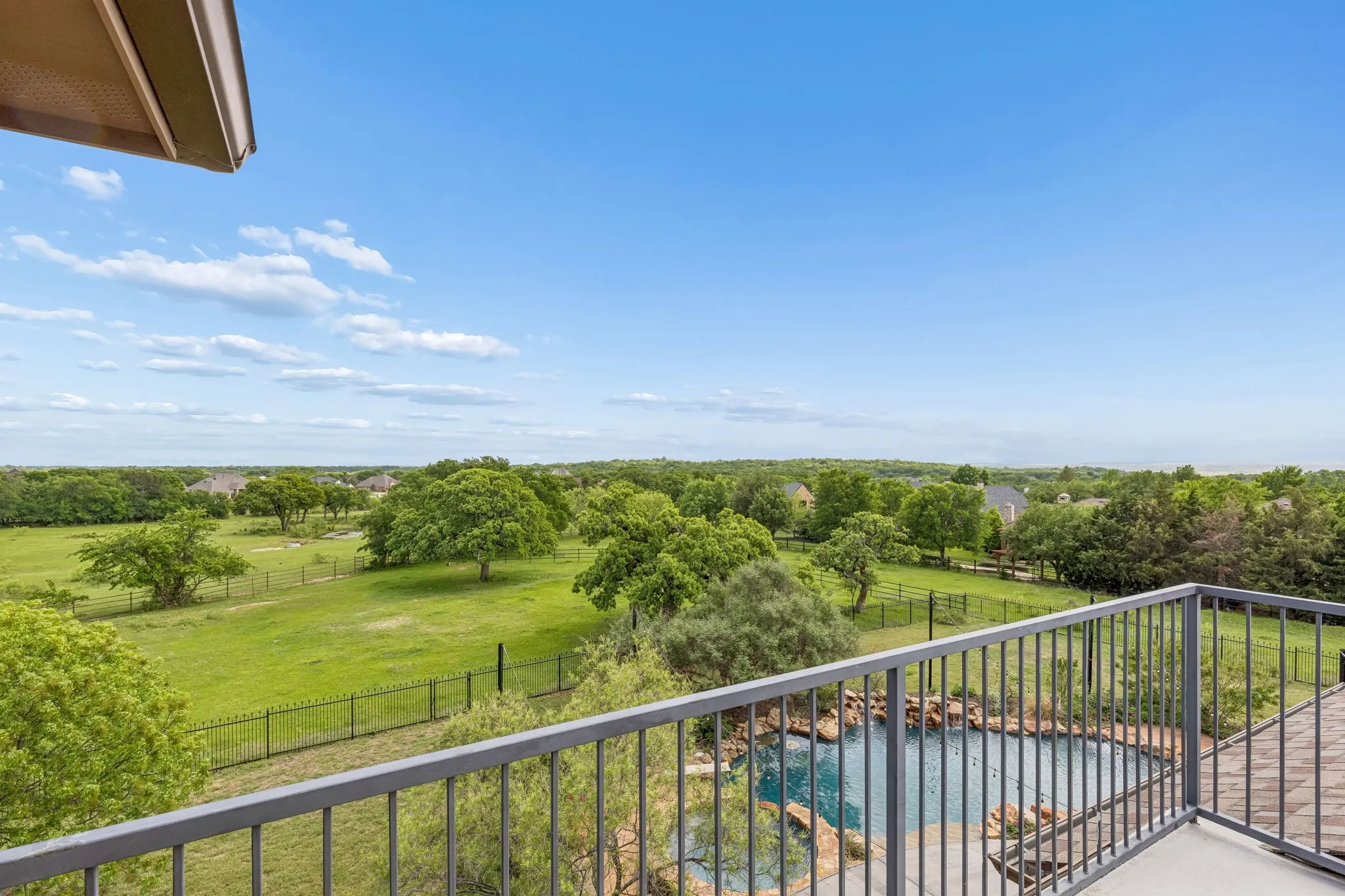 Expansive outdoor views from the property's balcony, overlooking a pool with rock features and green spaces