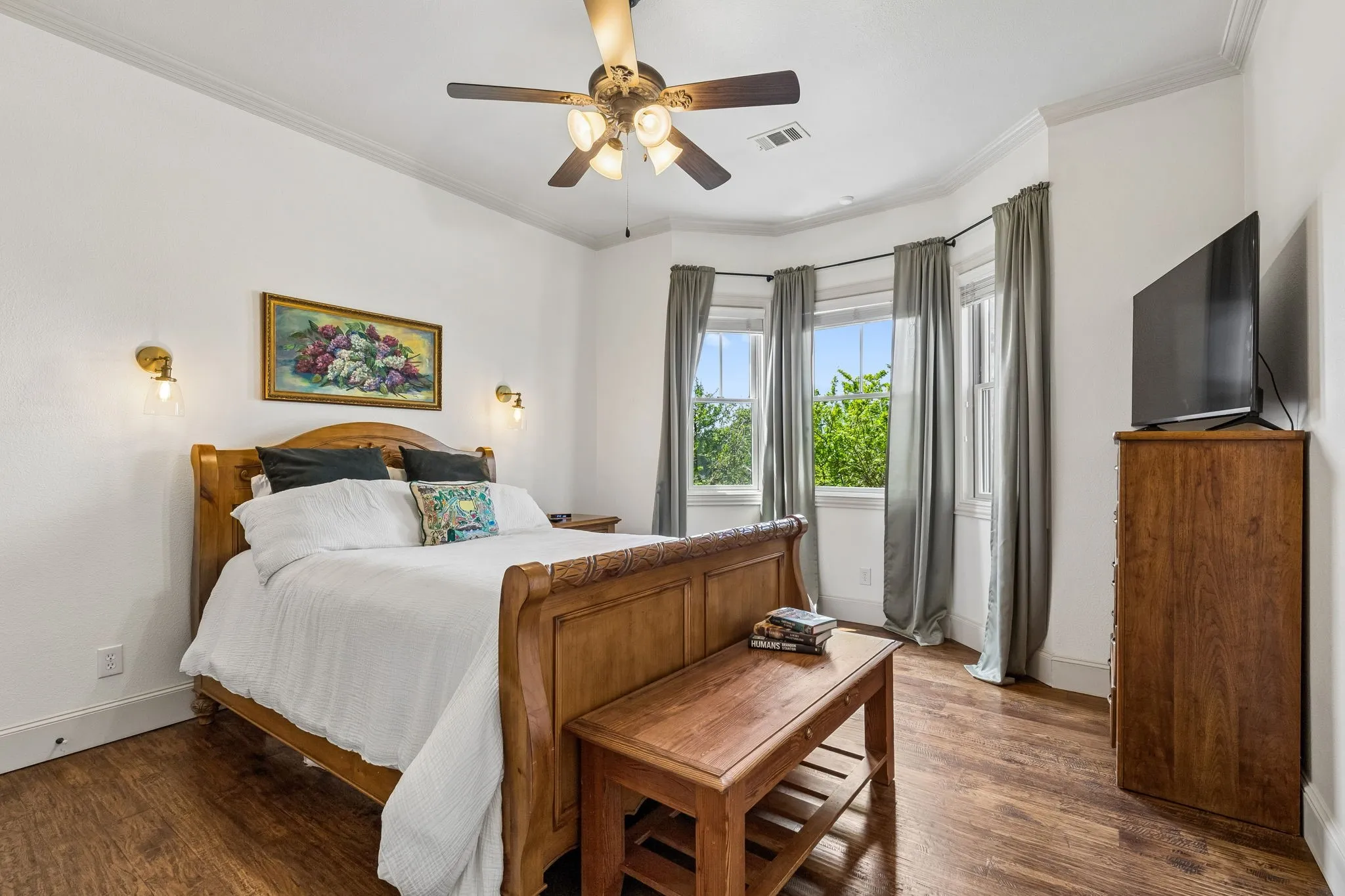 This room features hardwood flooring, a ceiling fan with integrated lighting, and multiple windows with draperies