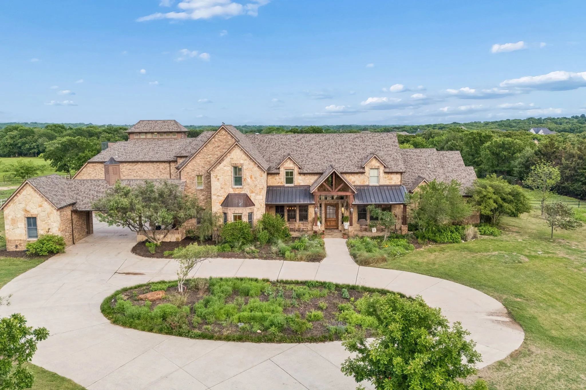 This property features a stone exterior, a covered entryway with exposed wood beams, and a paved circular driveway