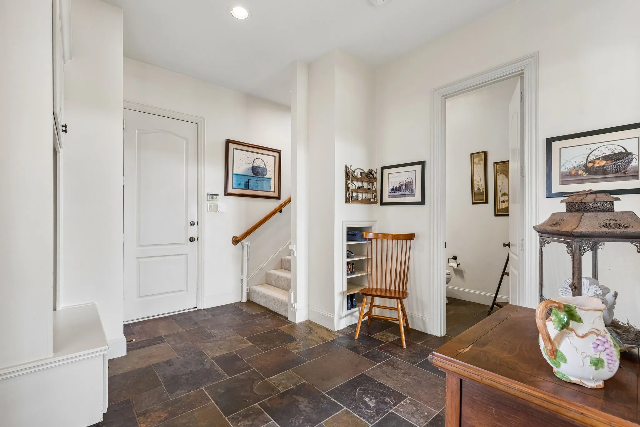The entryway features slate tile flooring, a white door, and a carpeted staircase with a wooden handrail