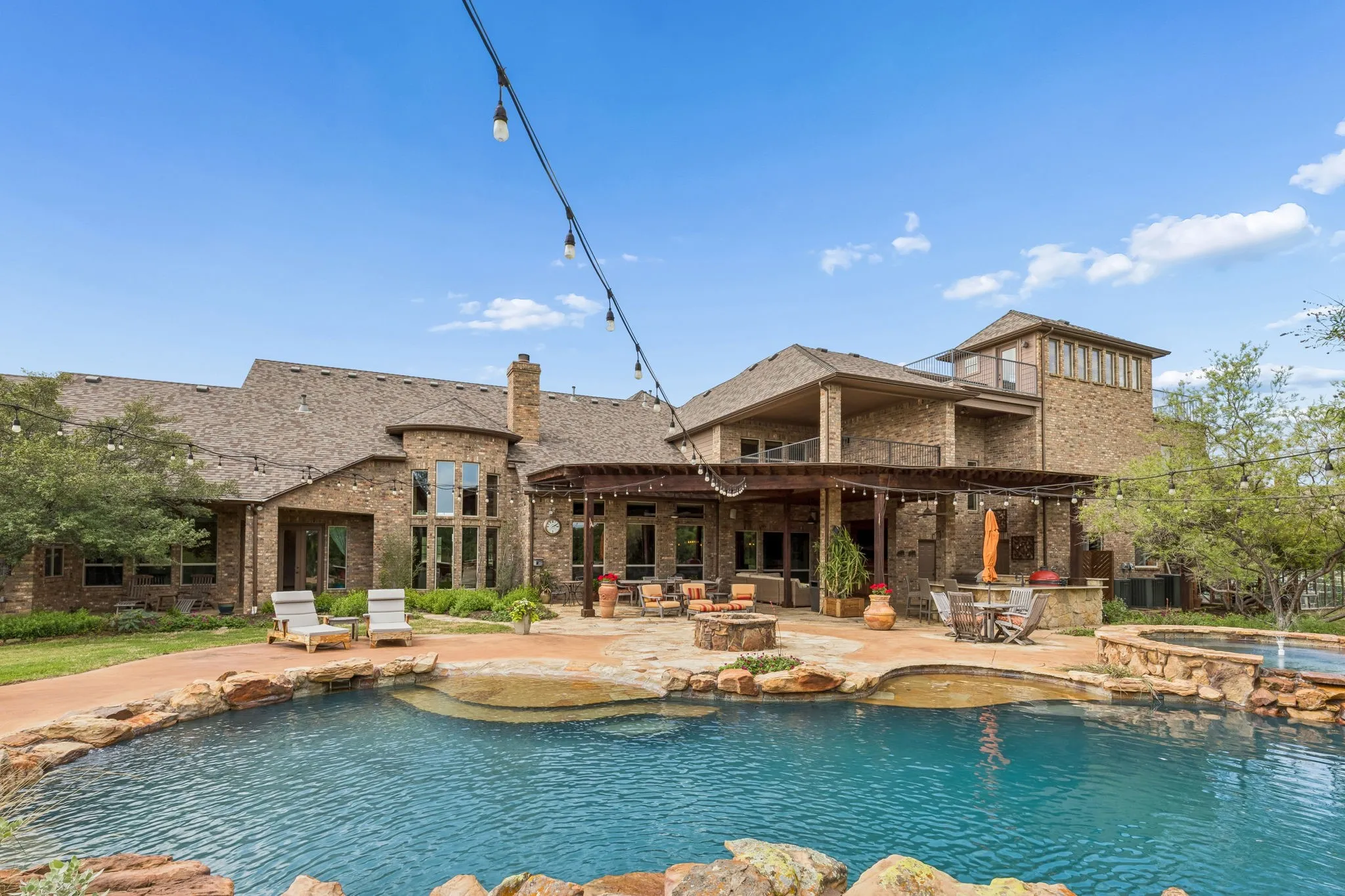 The property features a large outdoor pool with rock detailing, a spacious patio area with a pergola, and a built-in outdoor fire pit