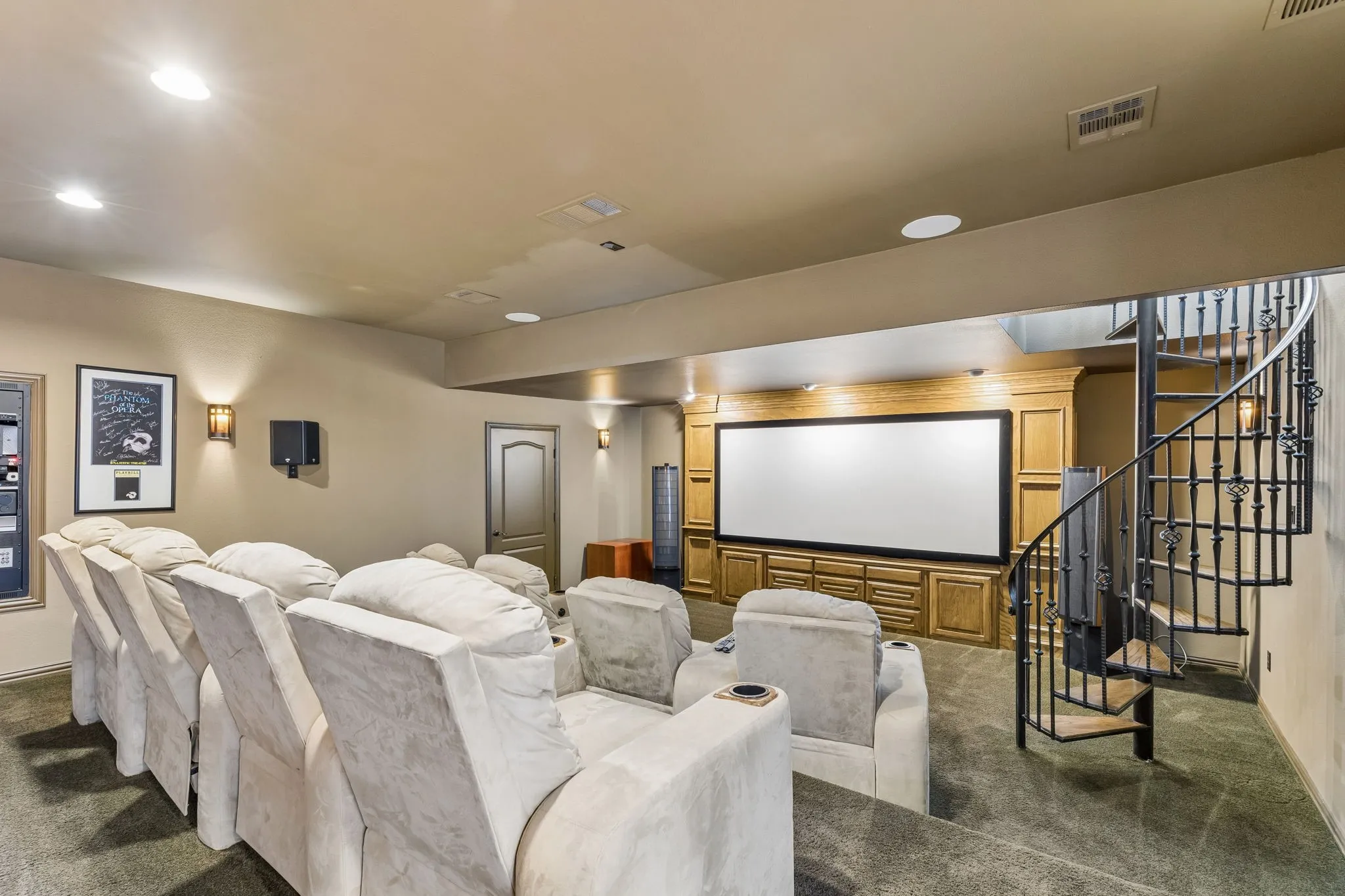 Entertainment room featuring a large projection screen, built-in wooden cabinetry, and a spiral staircase with wrought iron detailing