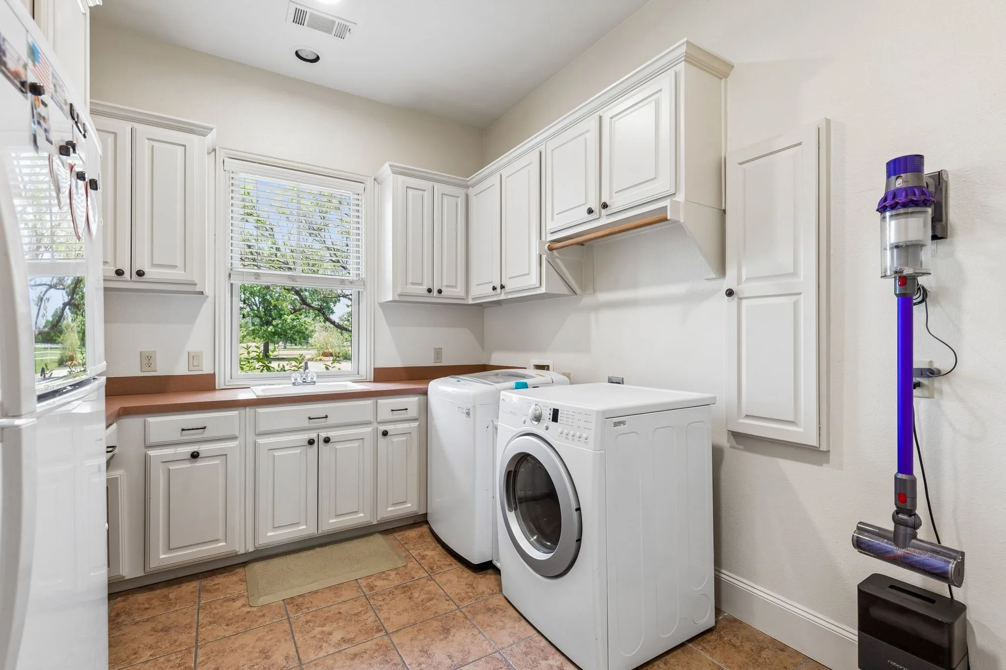 Utility room featuring white cabinetry, a window with blinds, and tiled flooring