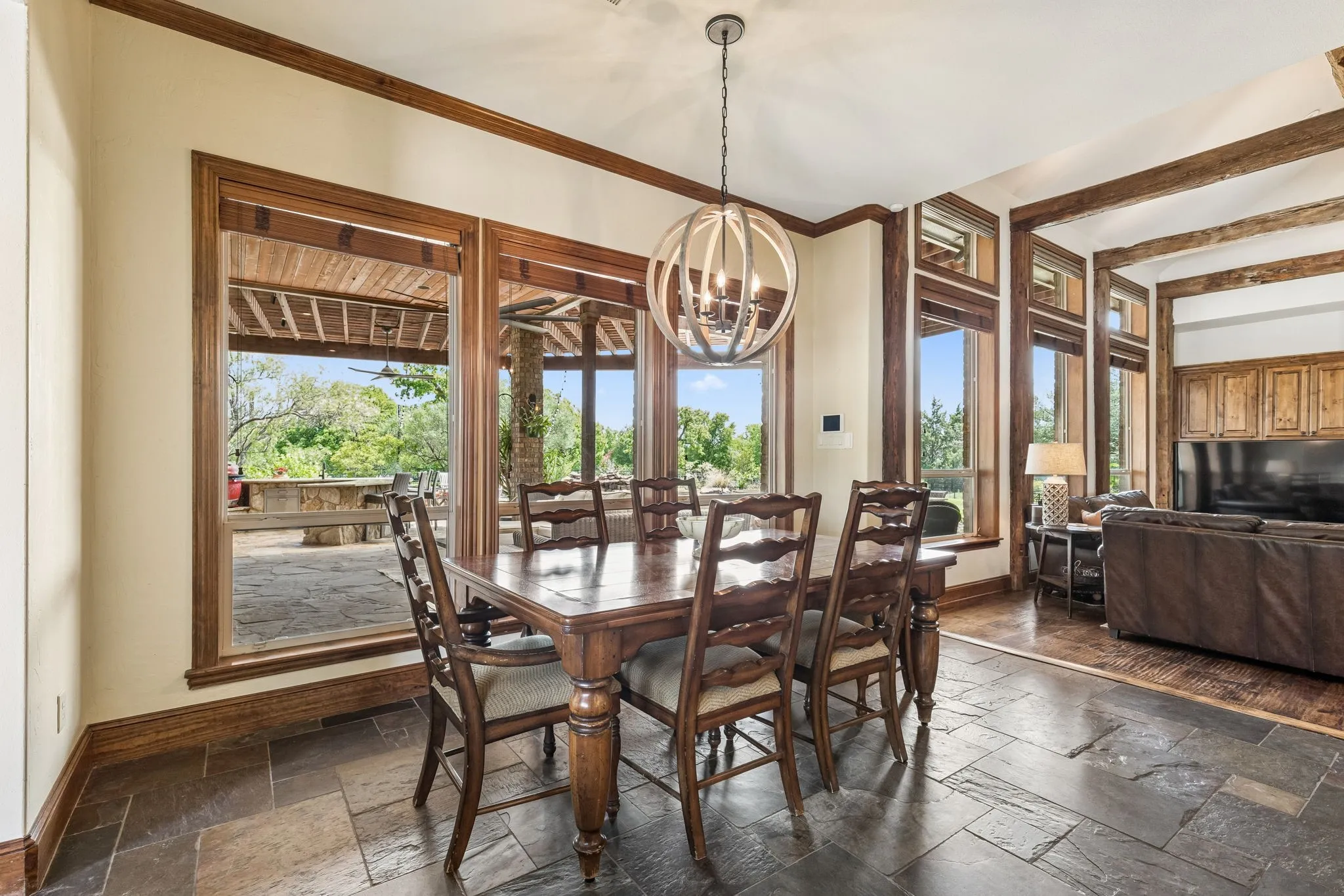 The dining area features stone tile flooring, a decorative chandelier, and large windows with rich wood trim