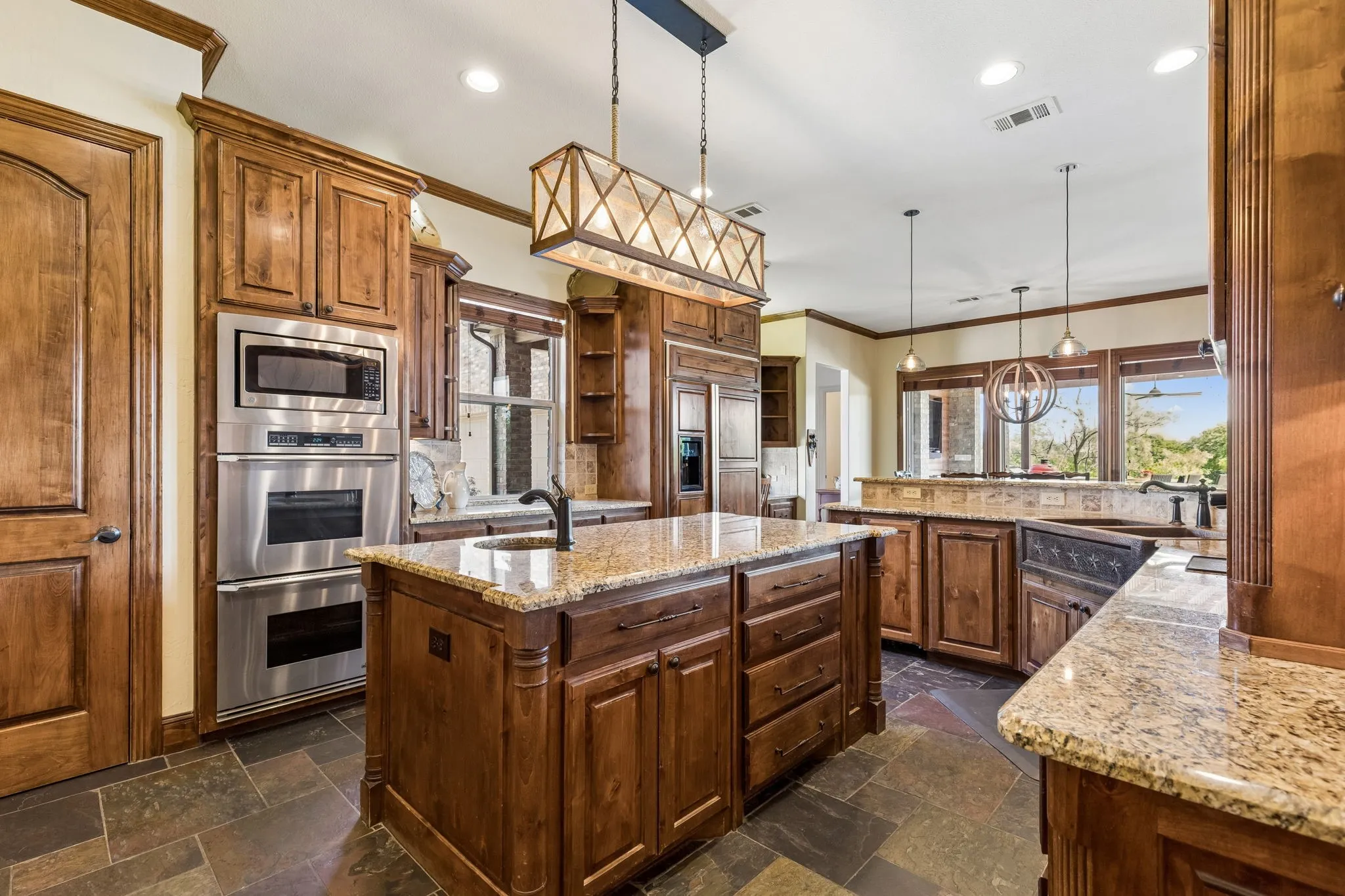Well-appointed kitchen featuring dark wood cabinetry, granite countertops, an island with a sink, and stainless steel appliances