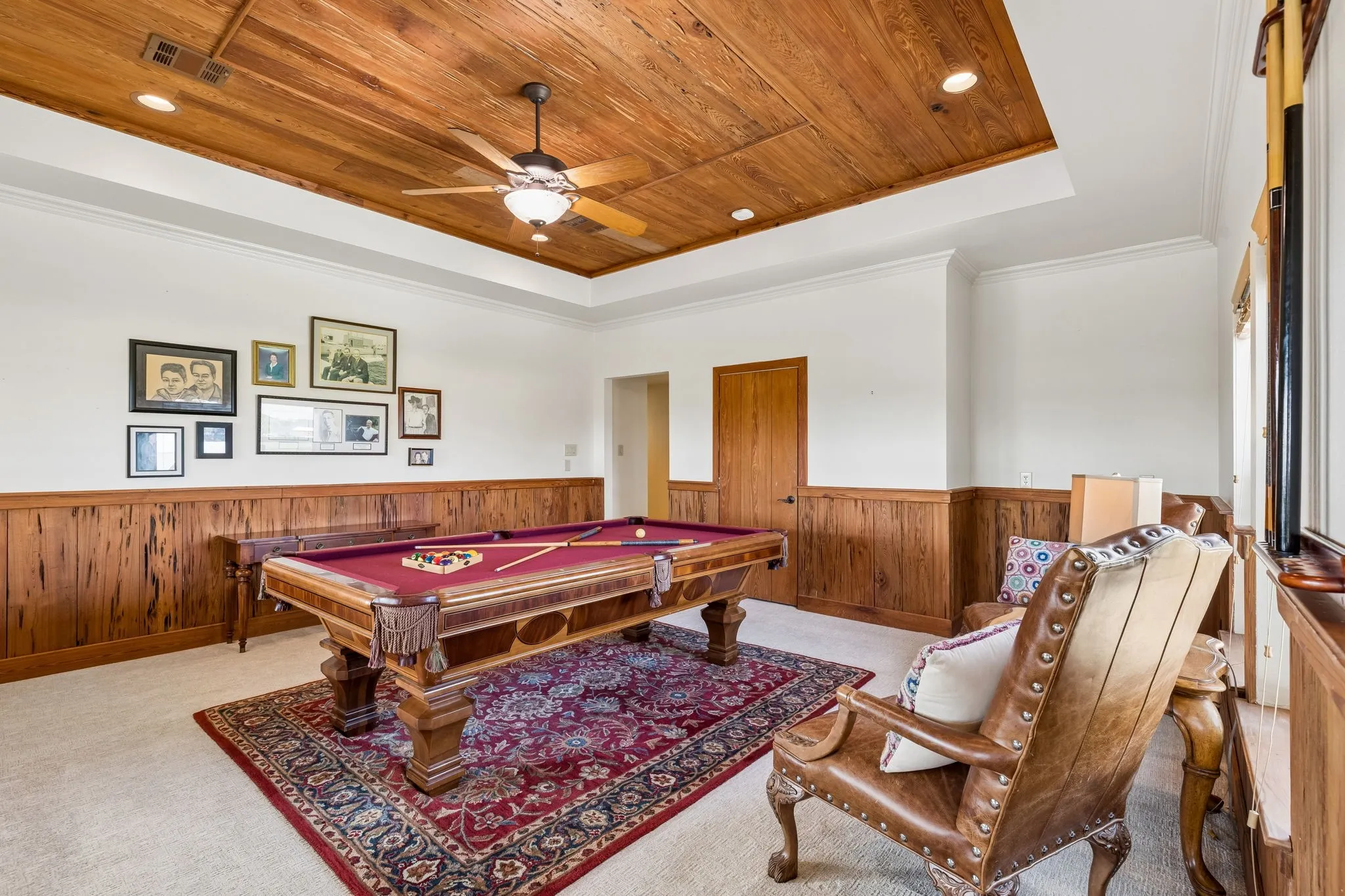 This room features a wooden paneled ceiling with a ceiling fan and recessed lighting, along with wooden wainscoting