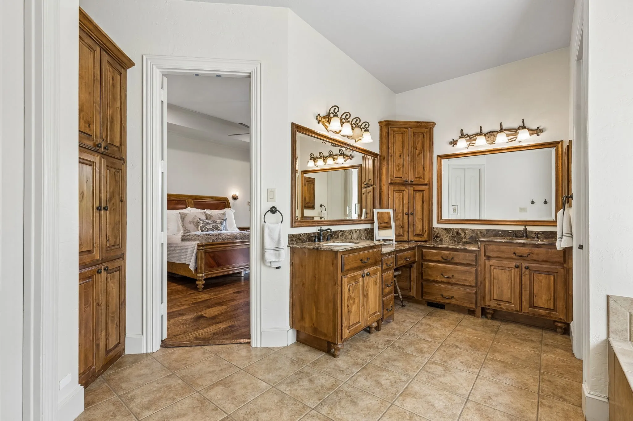 Well-appointed bathroom featuring tile flooring, extensive wood cabinetry, and dual vanity areas with marble countertops and framed mirrors