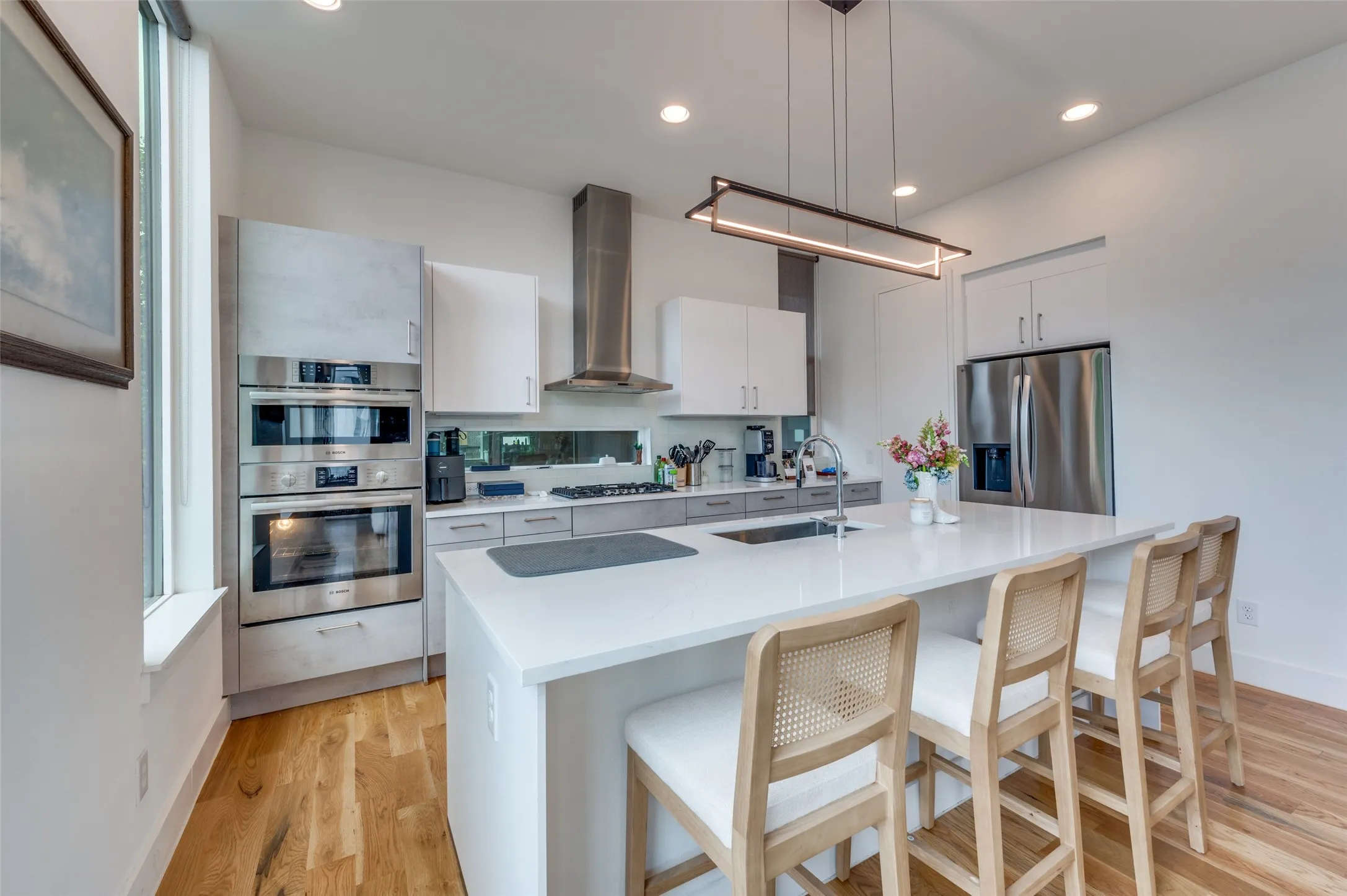 The kitchen features hardwood floors, white countertops, built-in stainless steel appliances, and a central island with seating