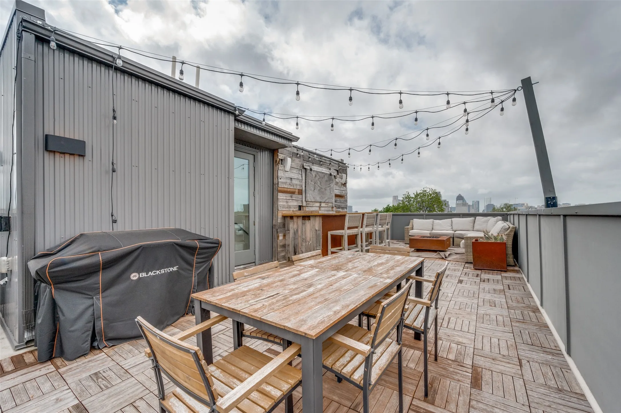 Spacious rooftop deck featuring string lighting, wood-look tiled flooring, and a cityscape view in the distance