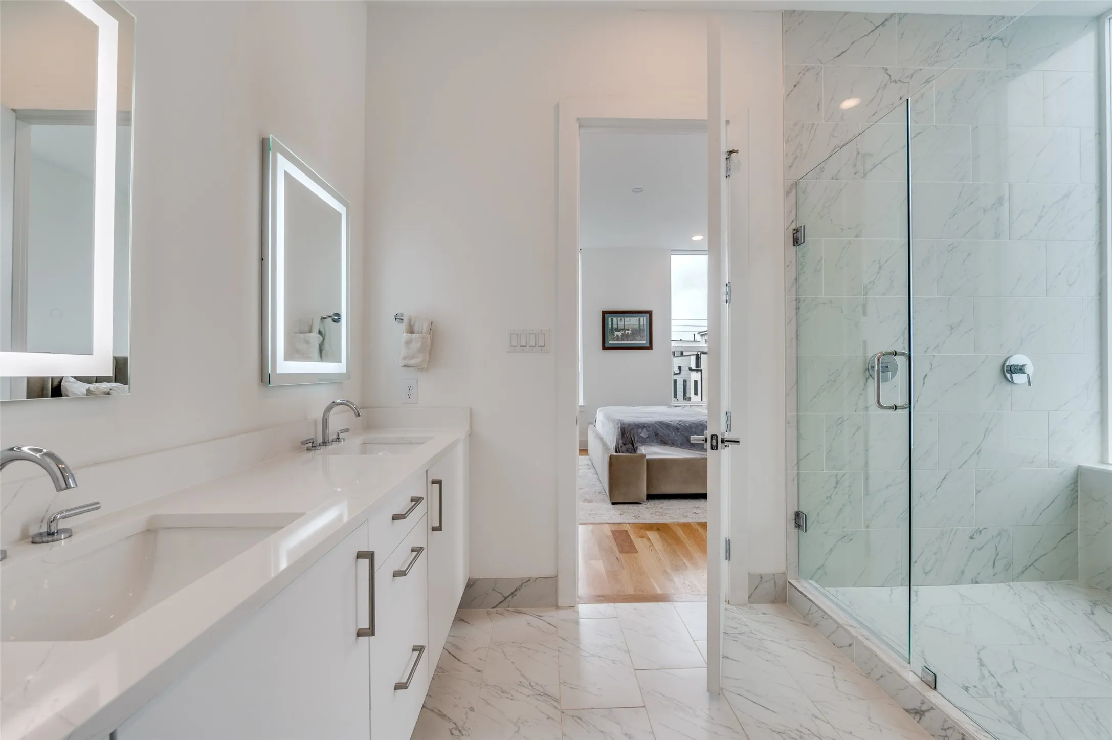 The bathroom features a double vanity with white countertops, integrated sinks, and illuminated mirrors